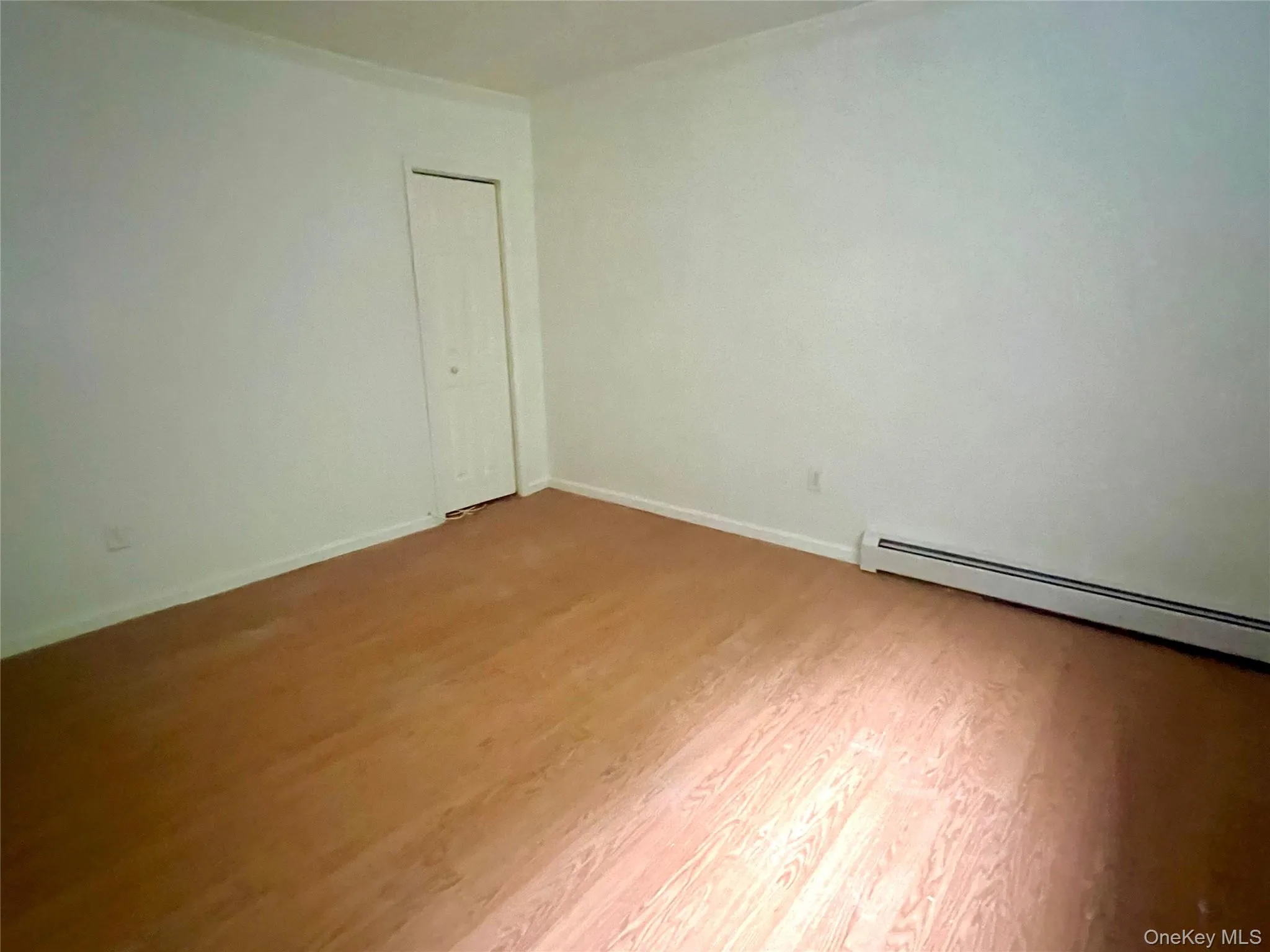 Unfurnished room with light wood finished floors and a baseboard heating unit Unfurnished room with light wood finished floors and a baseboard heating unit