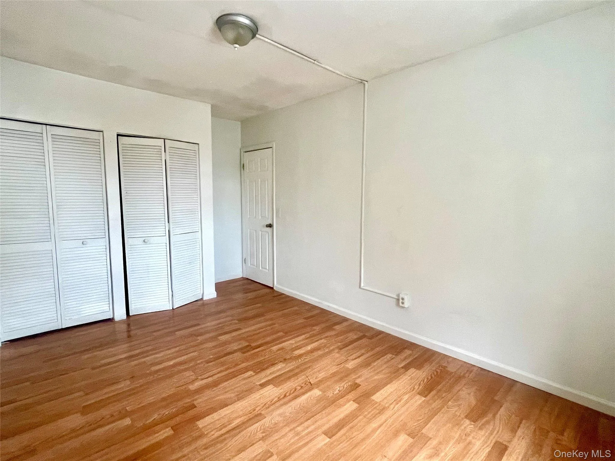 Unfurnished bedroom with light wood-type flooring and multiple closets Unfurnished bedroom with light wood-type flooring and multiple closets