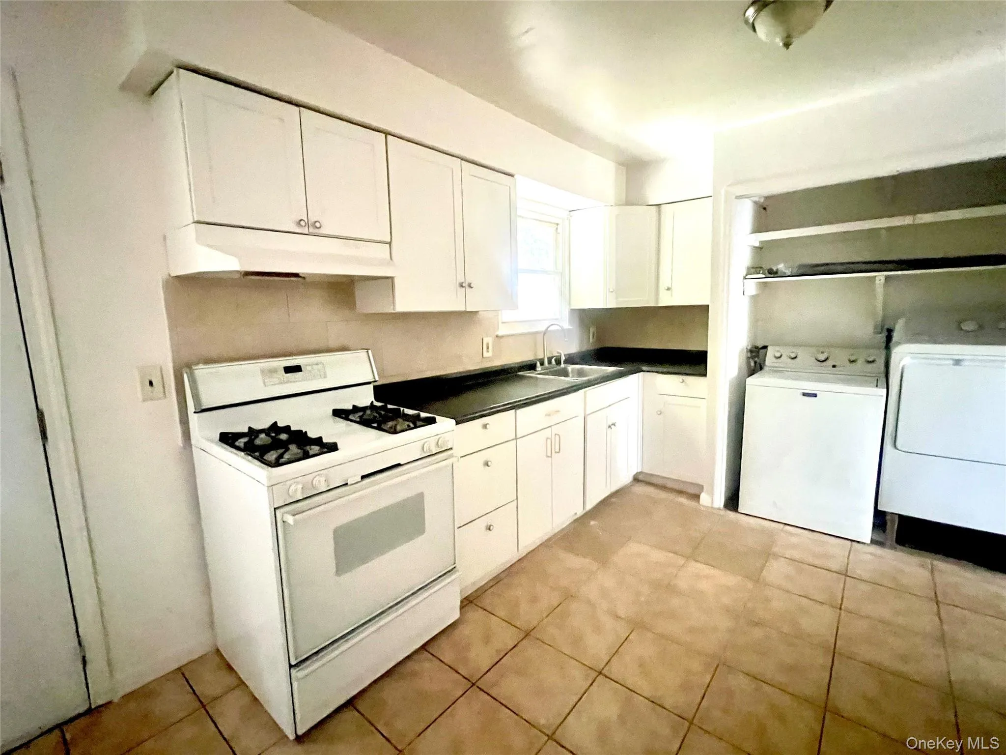 Kitchen featuring gas range gas stove, white cabinets, dark countertops, separate washer and dryer, and under cabinet range hood Kitchen featuring gas range gas stove, white cabinets, dark countertops, separate washer and dryer, and under cabinet range hood