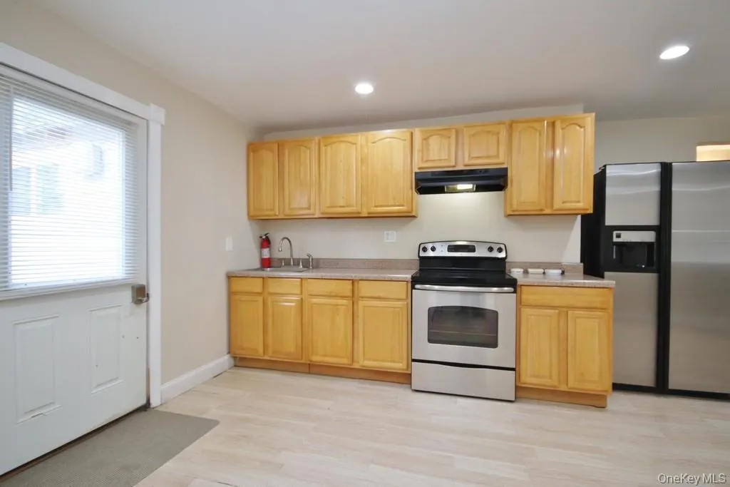 Kitchen featuring appliances with stainless steel finishes, light countertops, light brown cabinetry, under cabinet range hood, and light wood-style flooring Kitchen featuring appliances with stainless steel finishes, light countertops, light brown cabinetry, under cabinet range hood, and light wood-style flooring