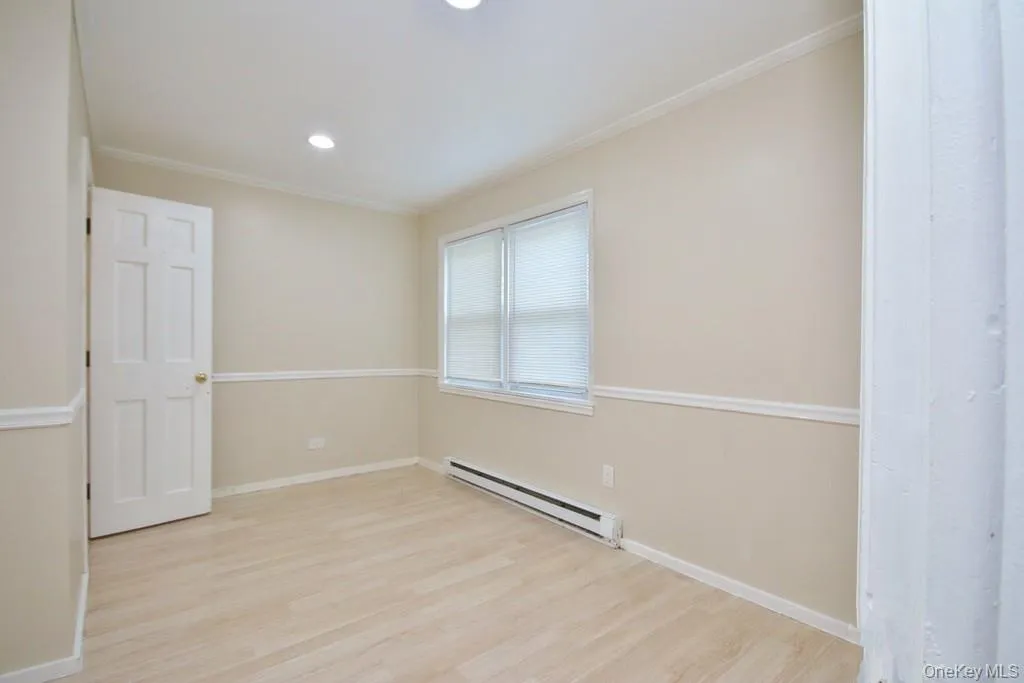 Unfurnished room with a baseboard radiator, light wood finished floors, crown molding, and recessed lighting Unfurnished room with a baseboard radiator, light wood finished floors, crown molding, and recessed lighting