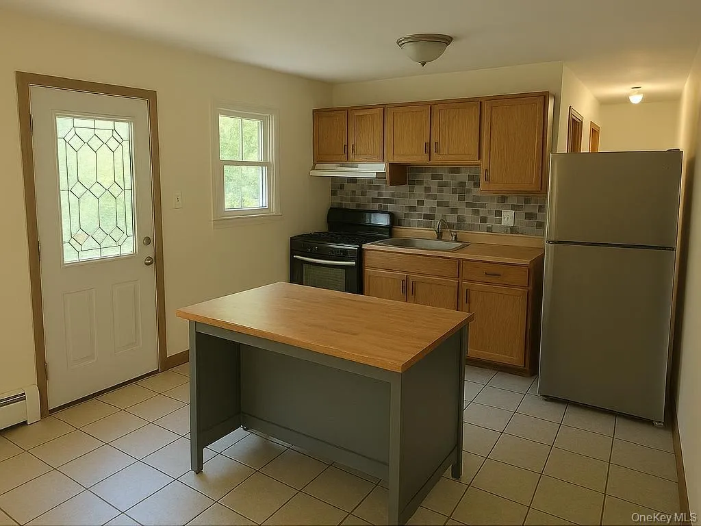 Kitchen with freestanding refrigerator, light countertops, black gas range, and light tile patterned floors Kitchen with freestanding refrigerator, light countertops, black gas range, and light tile patterned floors