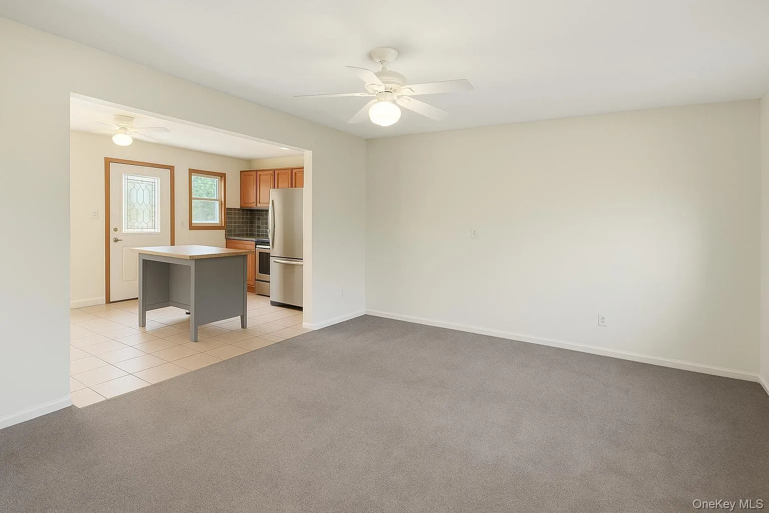 Unfurnished living room with light colored carpet, light tile patterned floors, and a ceiling fan Unfurnished living room with light colored carpet, light tile patterned floors, and a ceiling fan