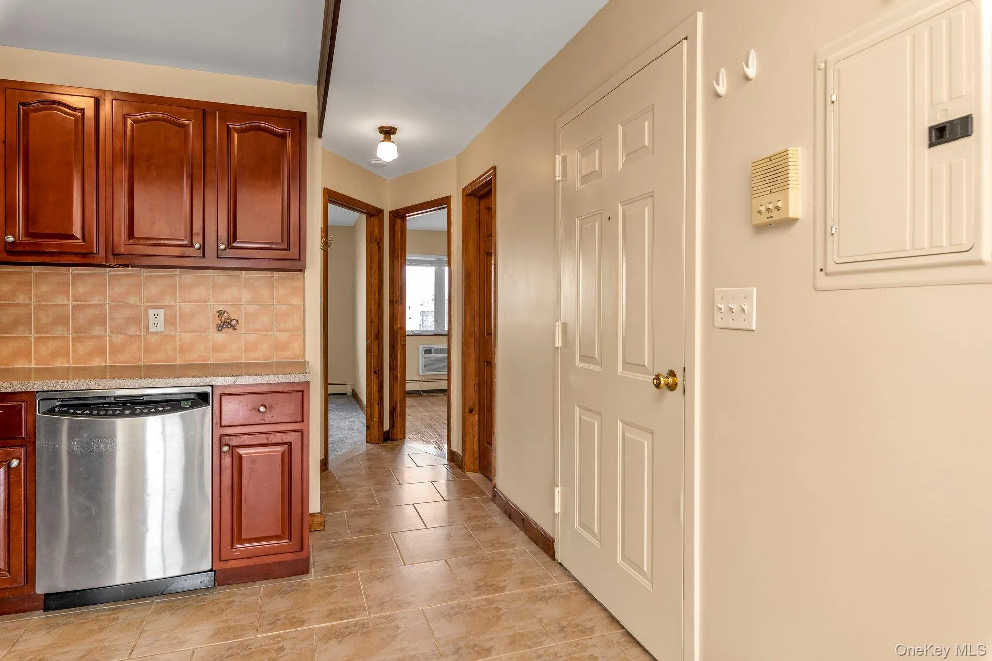 Kitchen featuring light countertops, electric panel, stainless steel dishwasher, decorative backsplash, and light tile patterned flooring Kitchen featuring light countertops, electric panel, stainless steel dishwasher, decorative backsplash, and light tile patterned flooring