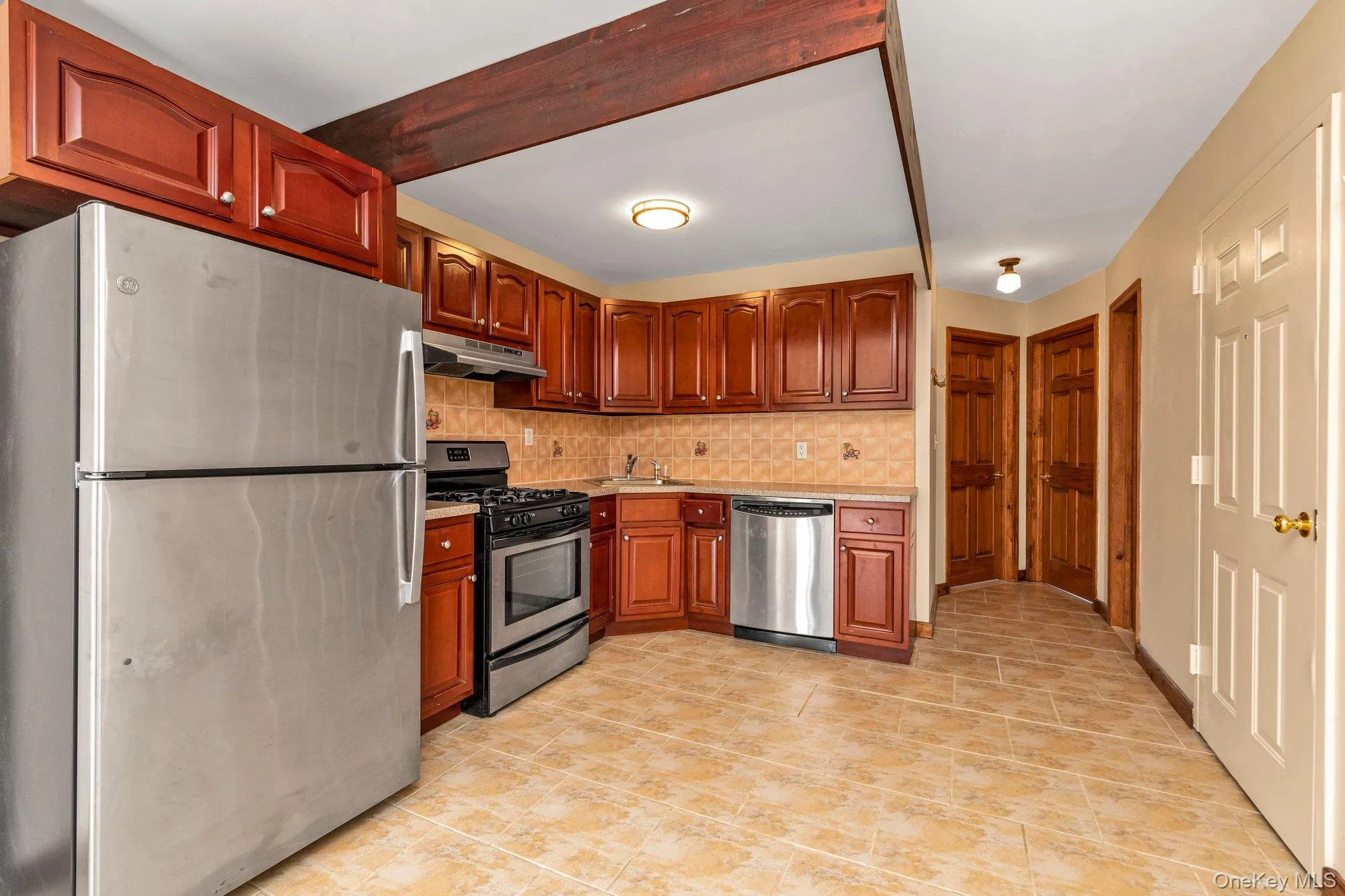 Kitchen with appliances with stainless steel finishes, tasteful backsplash, light countertops, under cabinet range hood, and brown cabinetry Kitchen with appliances with stainless steel finishes, tasteful backsplash, light countertops, under cabinet range hood, and brown cabinetry