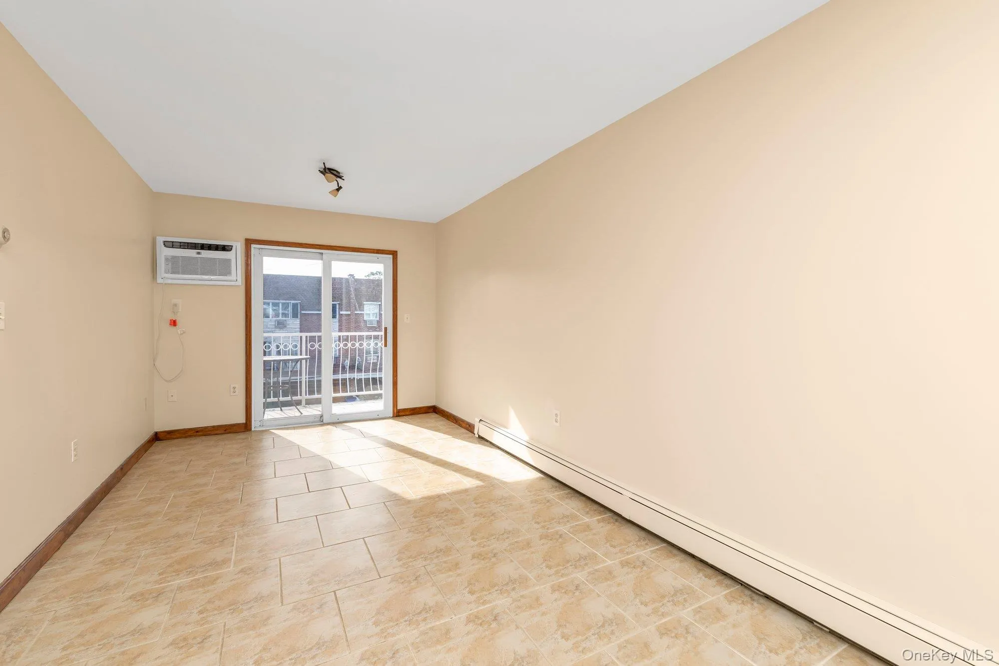 Empty room with a baseboard heating unit, an AC wall unit, and light tile patterned floors Empty room with a baseboard heating unit, an AC wall unit, and light tile patterned floors
