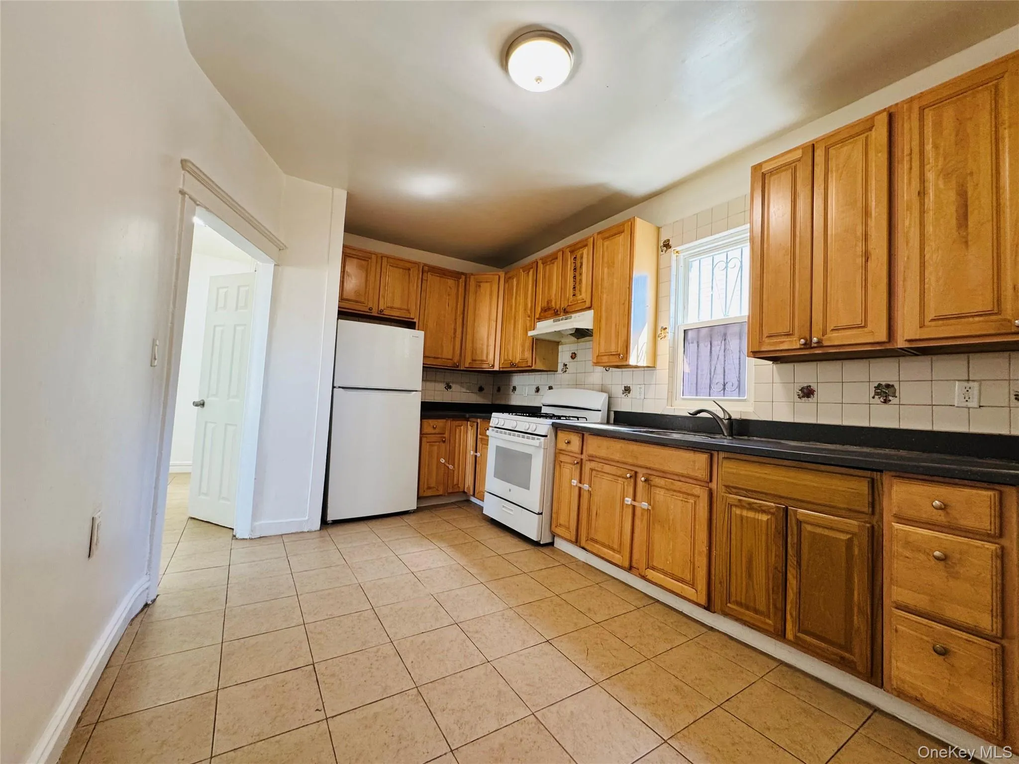 Kitchen featuring dark countertops, white appliances, decorative backsplash, and light tile patterned floors Kitchen featuring dark countertops, white appliances, decorative backsplash, and light tile patterned floors