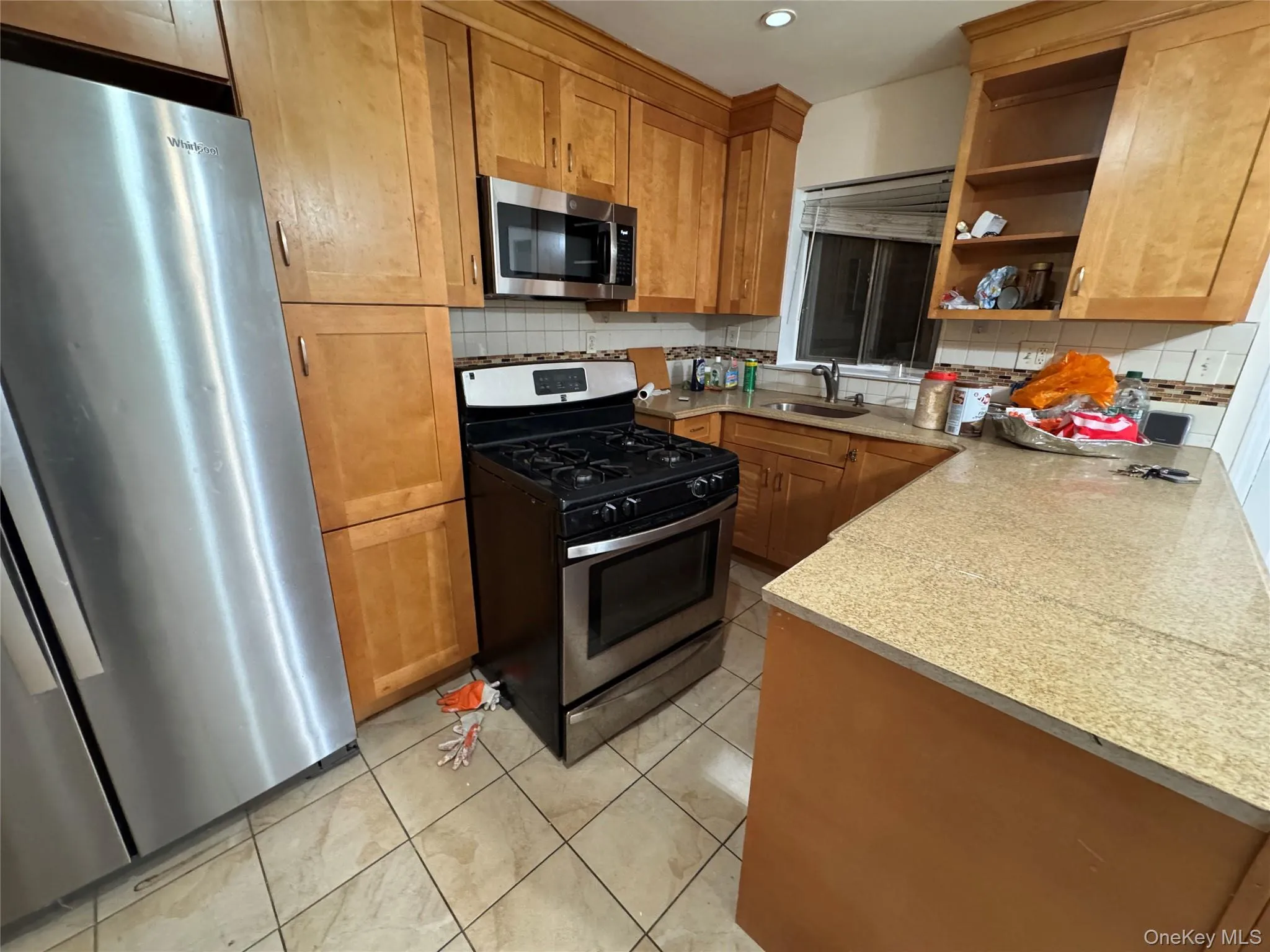 Kitchen featuring stainless steel appliances, light countertops, brown cabinetry, open shelves, and light tile patterned floors Kitchen featuring stainless steel appliances, light countertops, brown cabinetry, open shelves, and light tile patterned floors