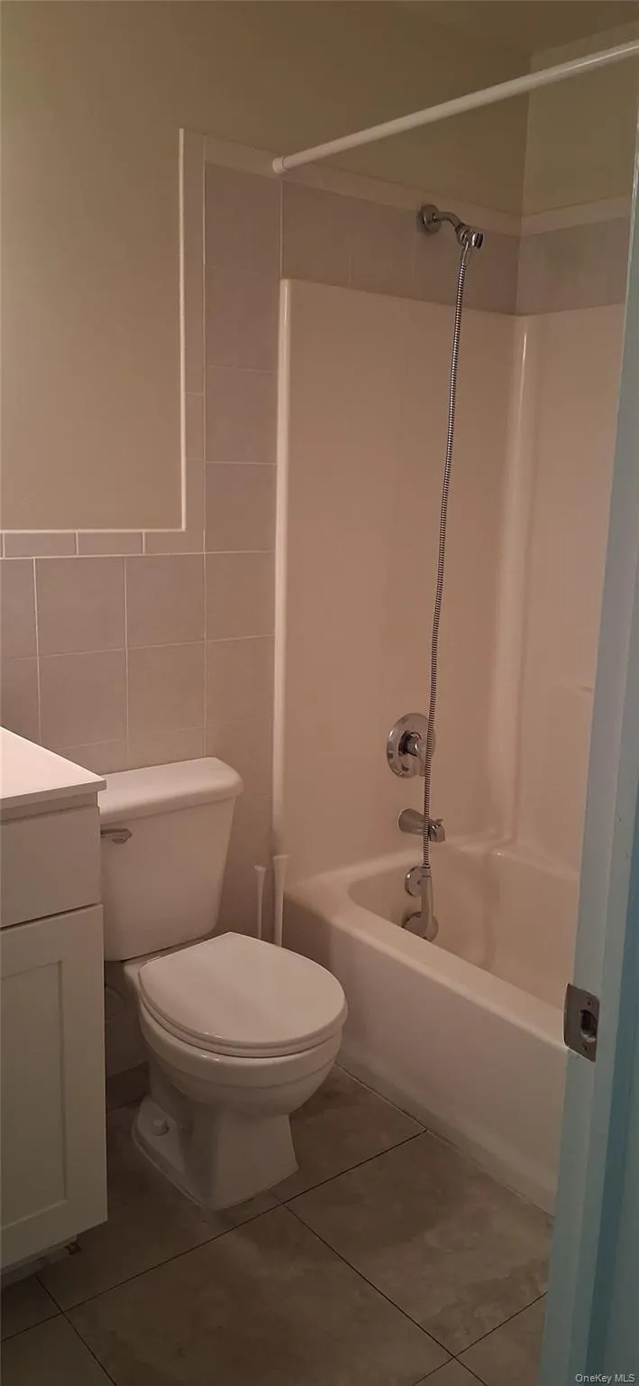 Bathroom with bathtub / shower combination, vanity, tile walls, and light tile patterned floors Bathroom with bathtub / shower combination, vanity, tile walls, and light tile patterned floors