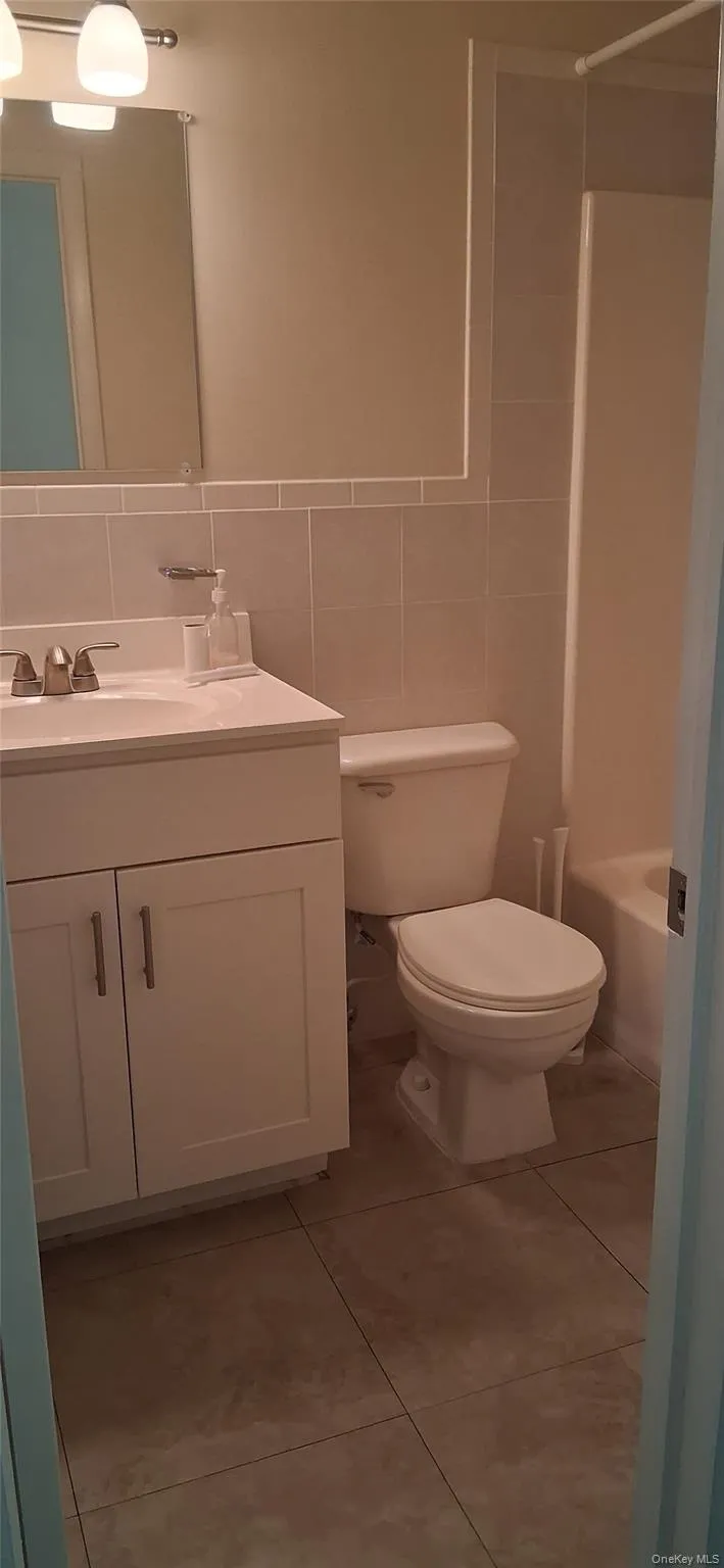 Full bath featuring tile walls, vanity, light tile patterned floors, washtub / shower combination, and backsplash Full bath featuring tile walls, vanity, light tile patterned floors, washtub / shower combination, and backsplash