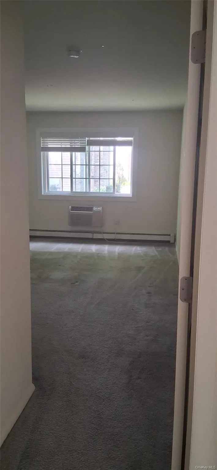 Unfurnished room with dark carpet, baseboard heating, and a wall mounted AC Unfurnished room with dark carpet, baseboard heating, and a wall mounted AC