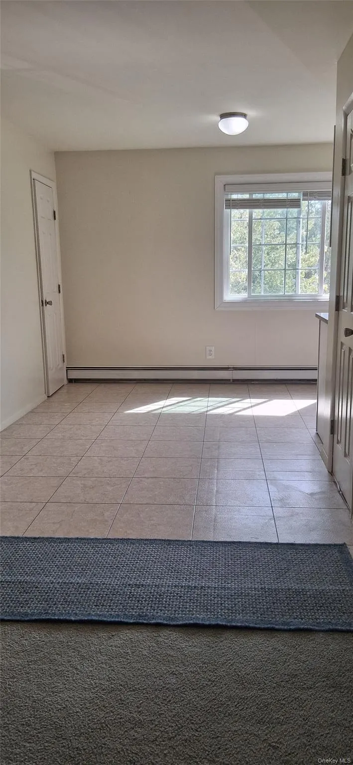 Empty room featuring light tile patterned flooring and a baseboard radiator Empty room featuring light tile patterned flooring and a baseboard radiator