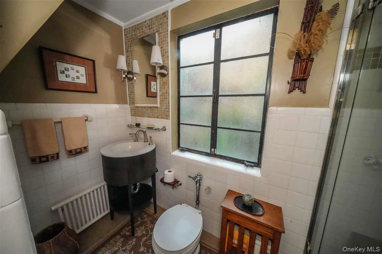 Bathroom with tile walls, a shower stall, radiator, a wainscoted wall, and crown molding Bathroom with tile walls, a shower stall, radiator, a wainscoted wall, and crown molding
