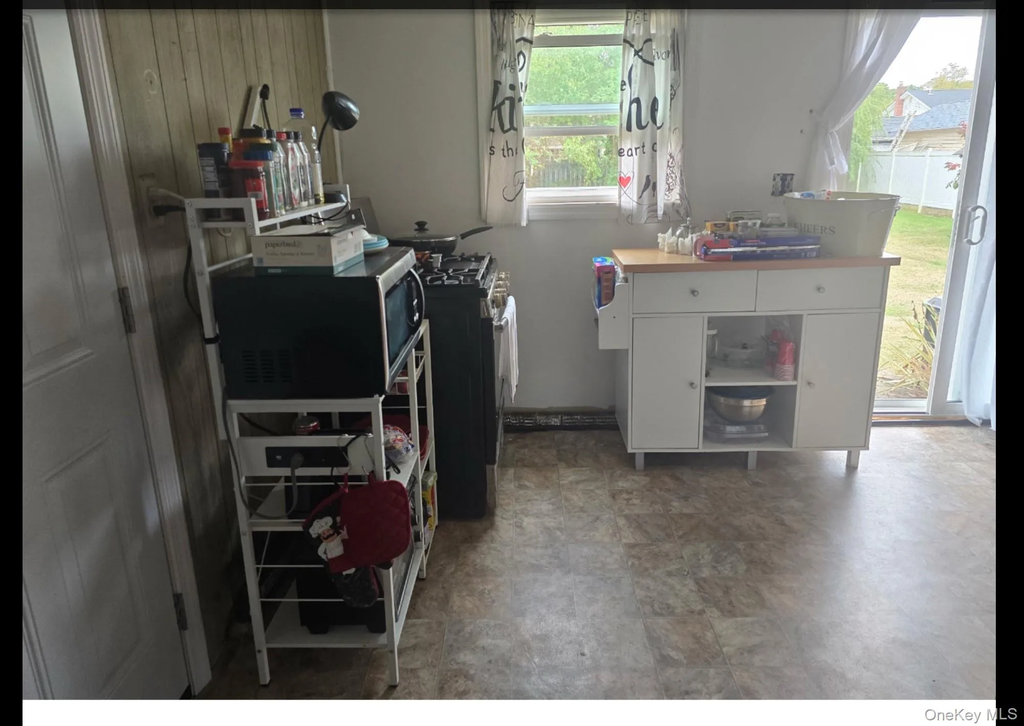 Kitchen with stainless steel microwave, white cabinetry, open shelves, and stone finish floors Kitchen with stainless steel microwave, white cabinetry, open shelves, and stone finish floors