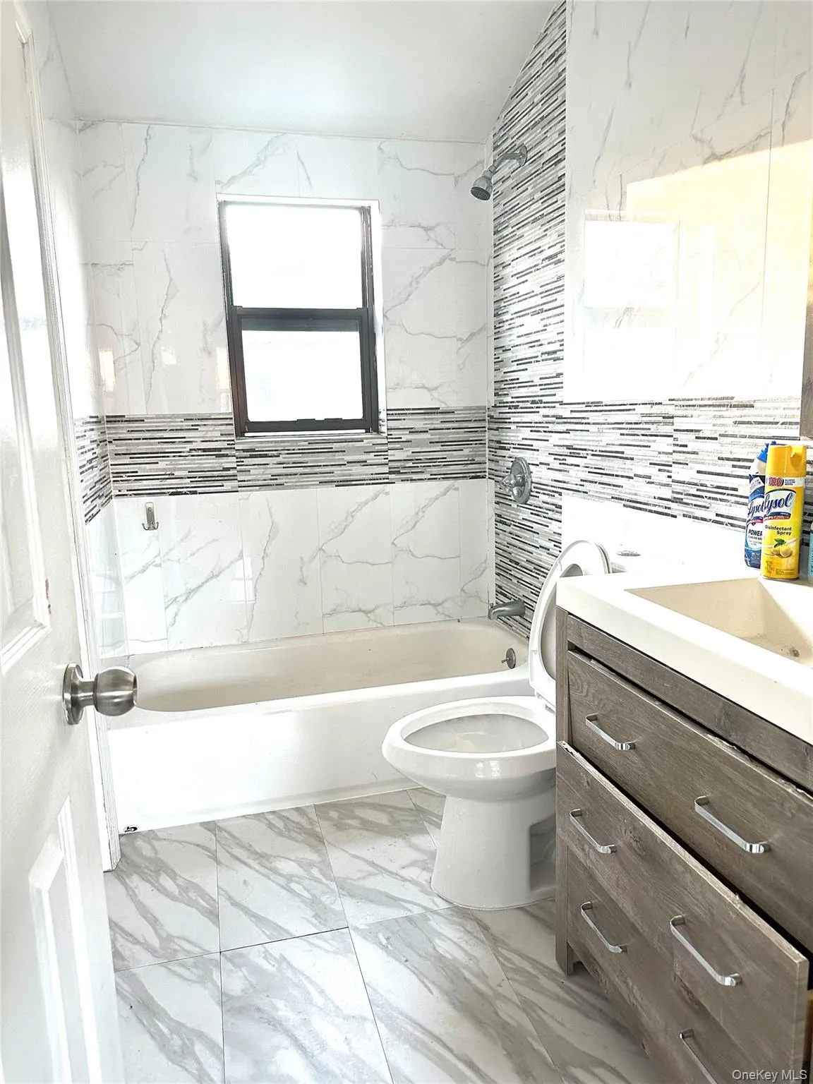 Bathroom with vanity, light marble finish flooring, shower / bathtub combination, and tile walls Bathroom with vanity, light marble finish flooring, shower / bathtub combination, and tile walls