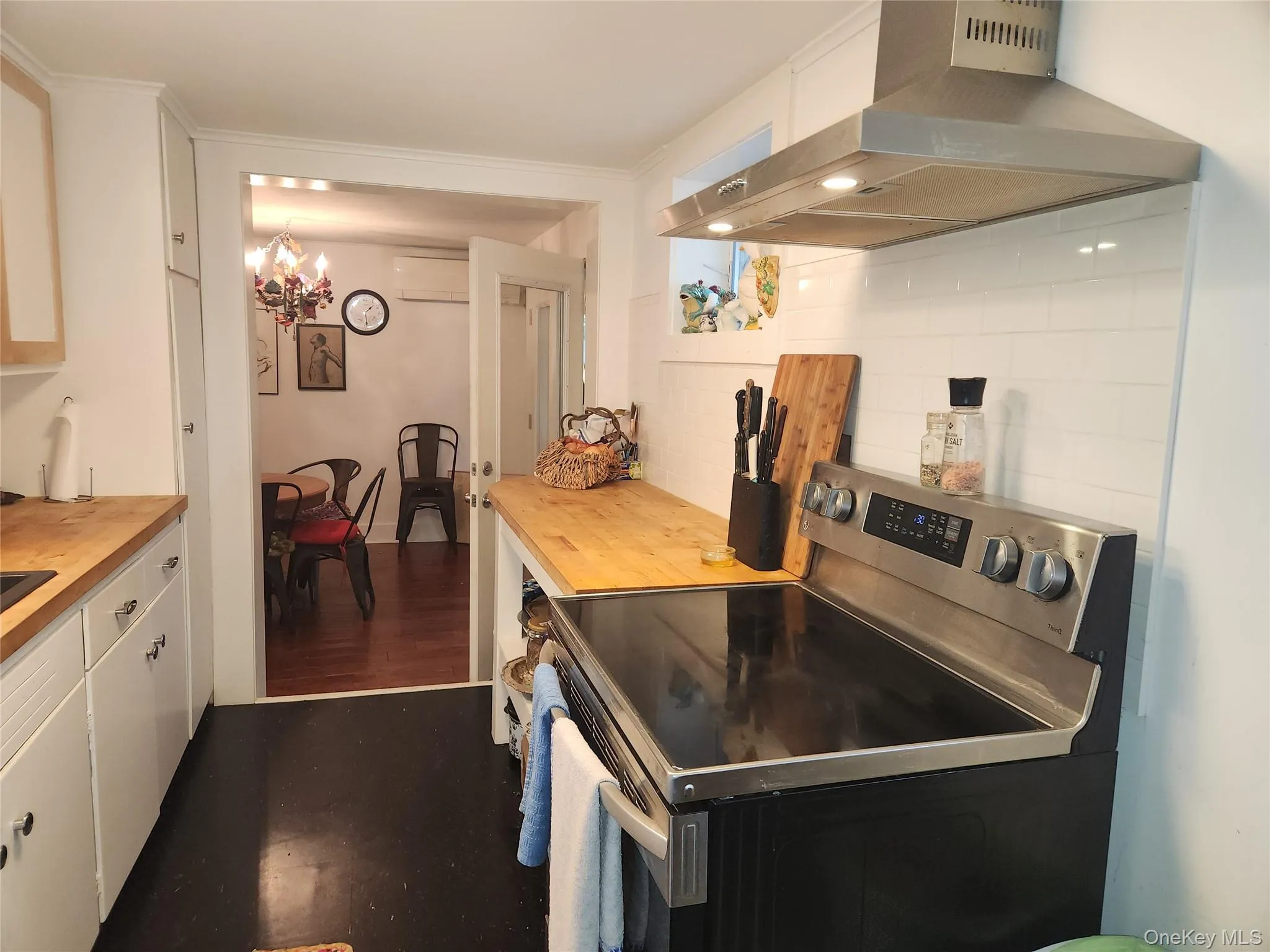 Kitchen featuring stainless steel electric stove, tasteful backsplash, ventilation hood, white cabinetry, and butcher block counters Kitchen featuring stainless steel electric stove, tasteful backsplash, ventilation hood, white cabinetry, and butcher block counters