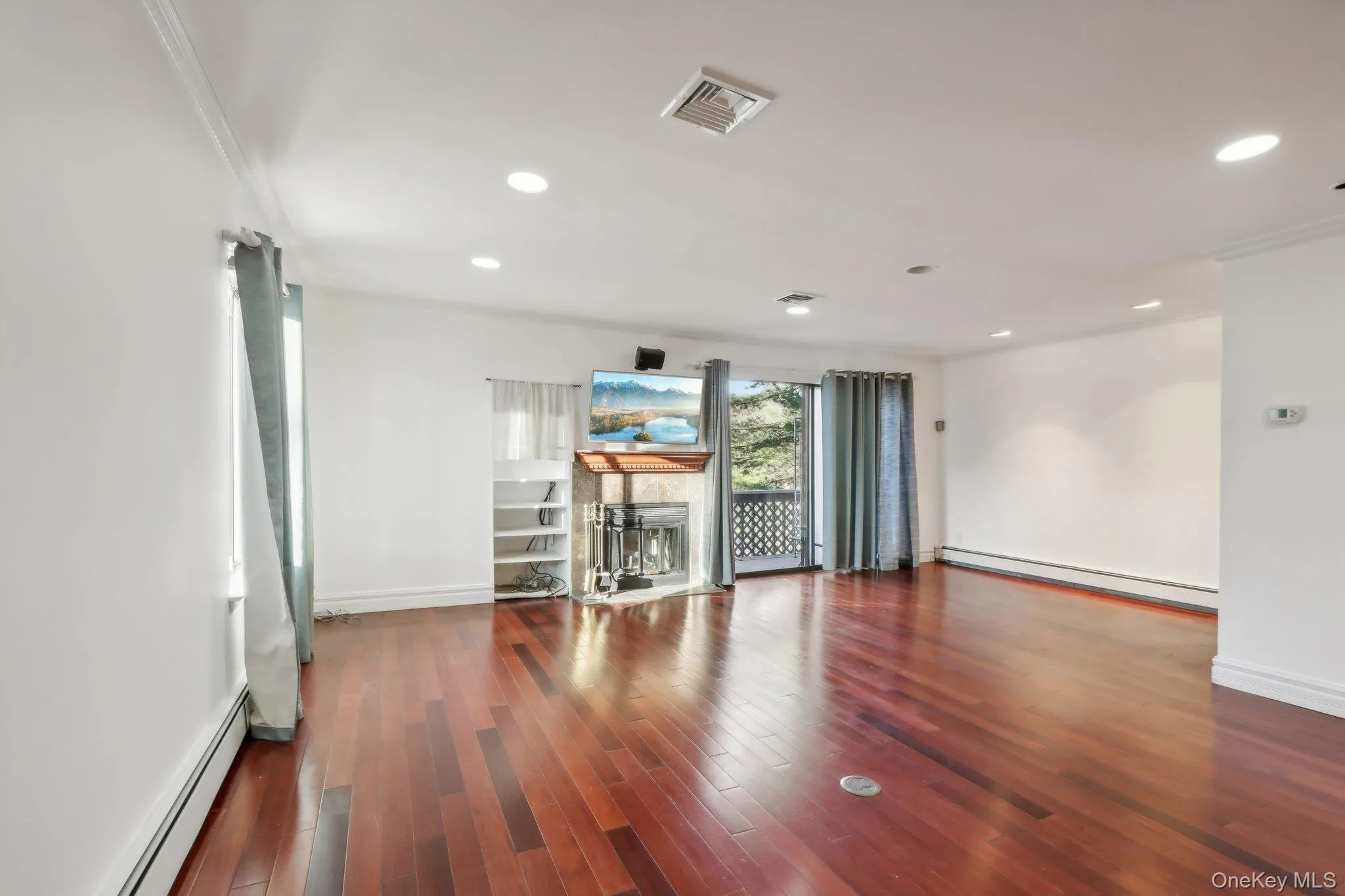 Unfurnished room featuring a baseboard radiator, dark wood-style flooring, a fireplace, and recessed lighting Unfurnished room featuring a baseboard radiator, dark wood-style flooring, a fireplace, and recessed lighting