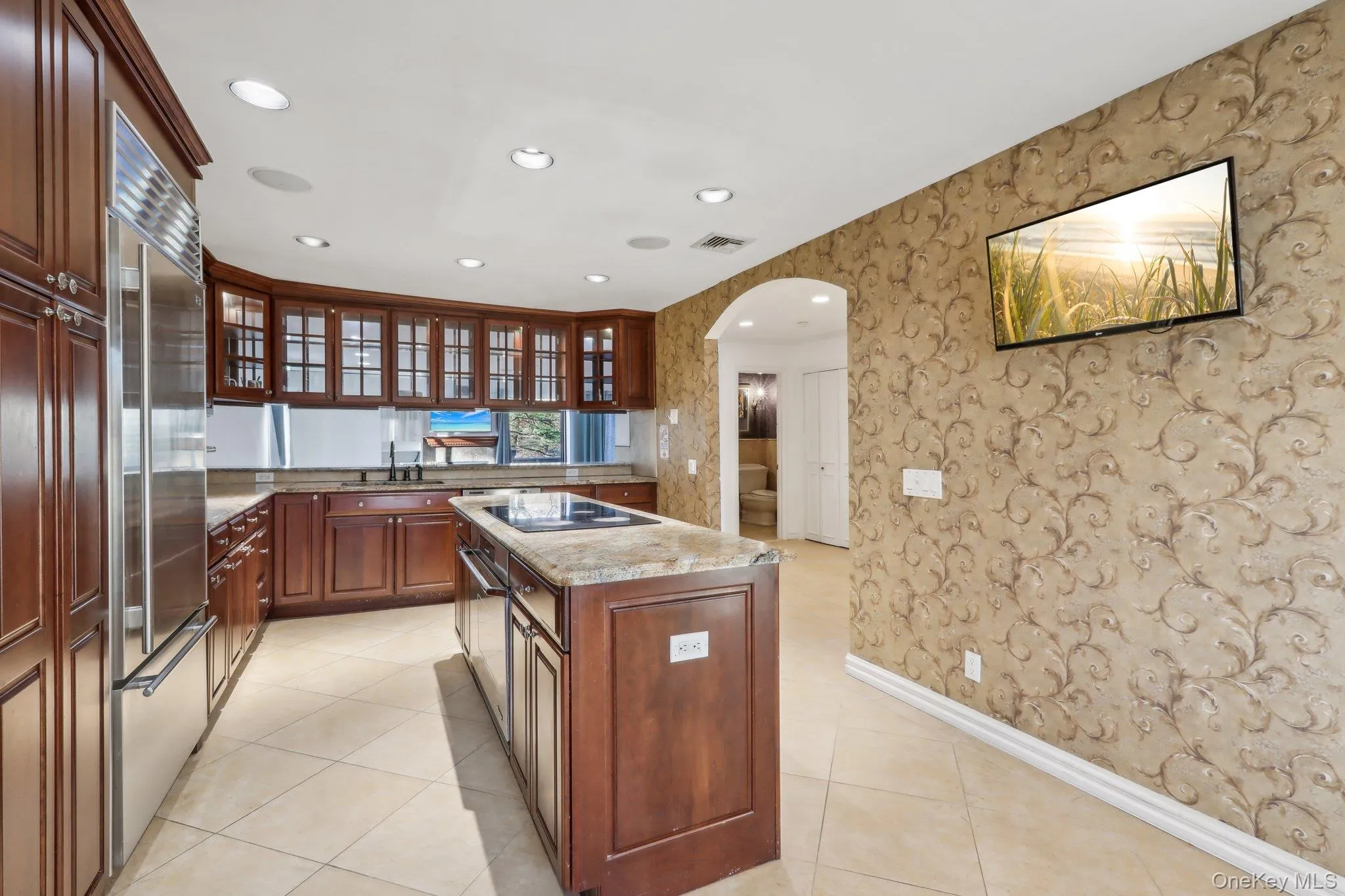 Kitchen with wallpapered walls, arched walkways, recessed lighting, a center island, and glass insert cabinets Kitchen with wallpapered walls, arched walkways, recessed lighting, a center island, and glass insert cabinets