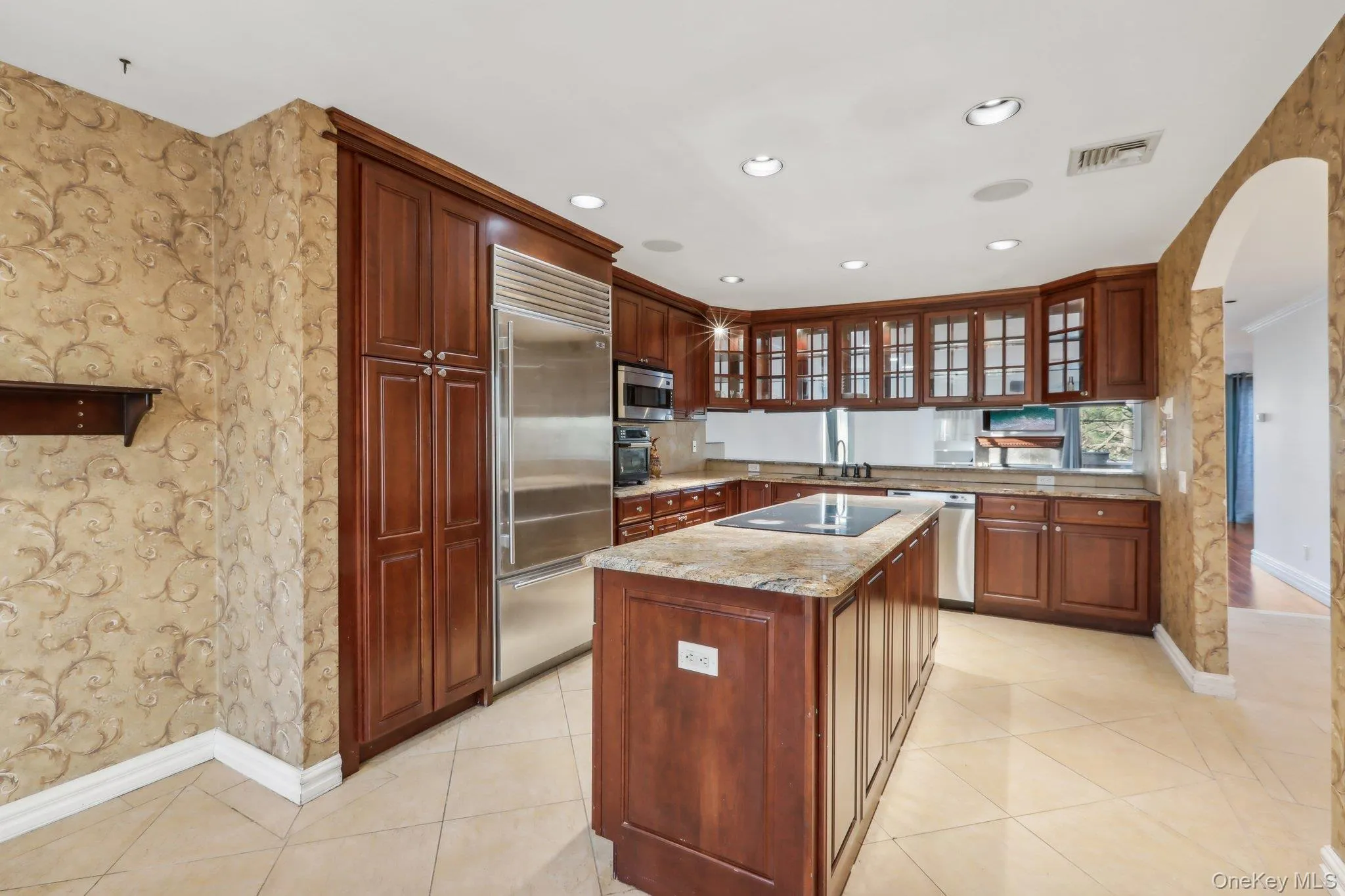 Kitchen featuring wallpapered walls, glass insert cabinets, arched walkways, appliances with stainless steel finishes, and recessed lighting Kitchen featuring wallpapered walls, glass insert cabinets, arched walkways, appliances with stainless steel finishes, and recessed lighting
