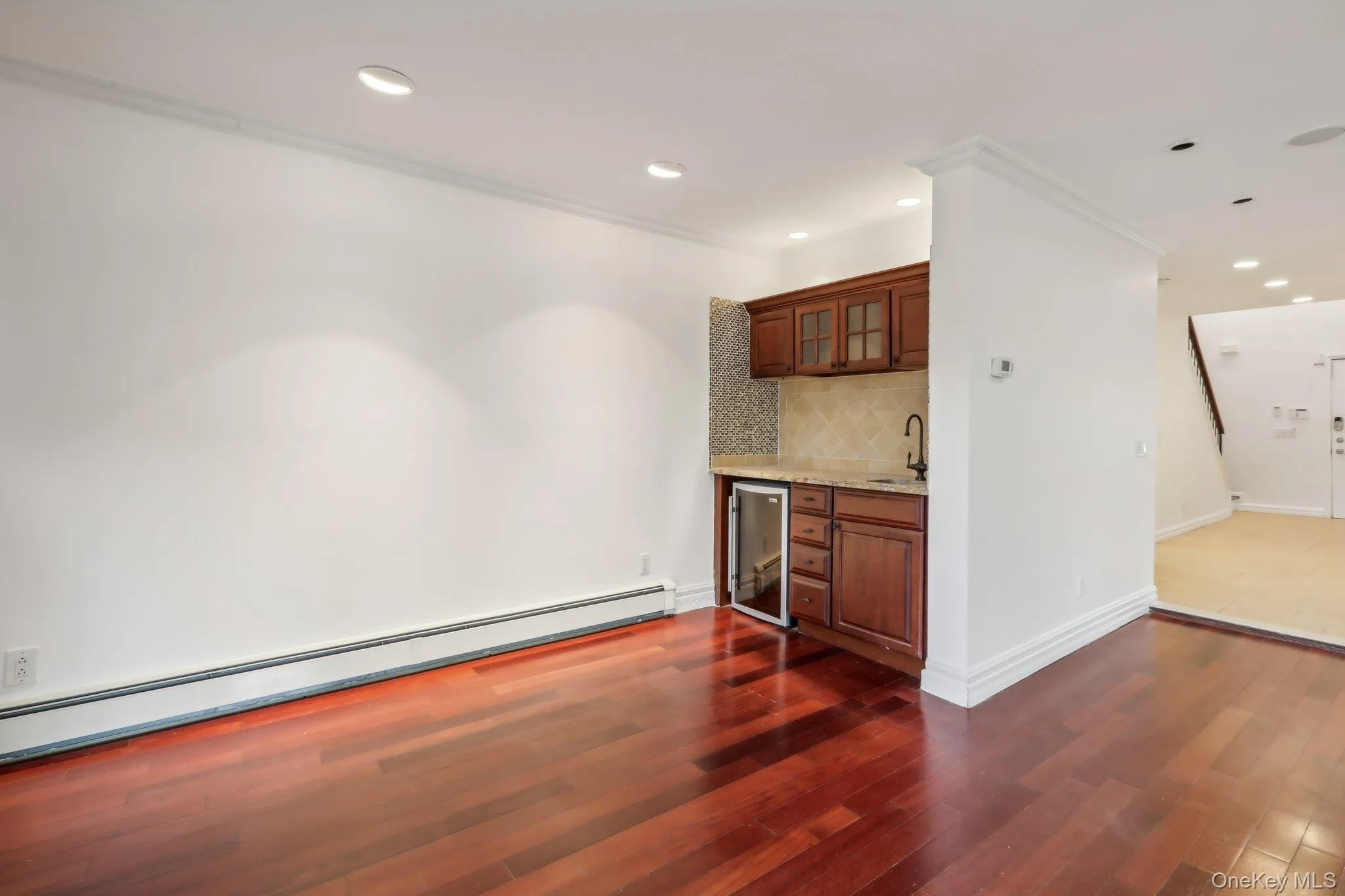 Indoor wet bar with baseboard heating, glass insert cabinets, brown cabinetry, tasteful backsplash, and dark wood-type flooring Indoor wet bar with baseboard heating, glass insert cabinets, brown cabinetry, tasteful backsplash, and dark wood-type flooring