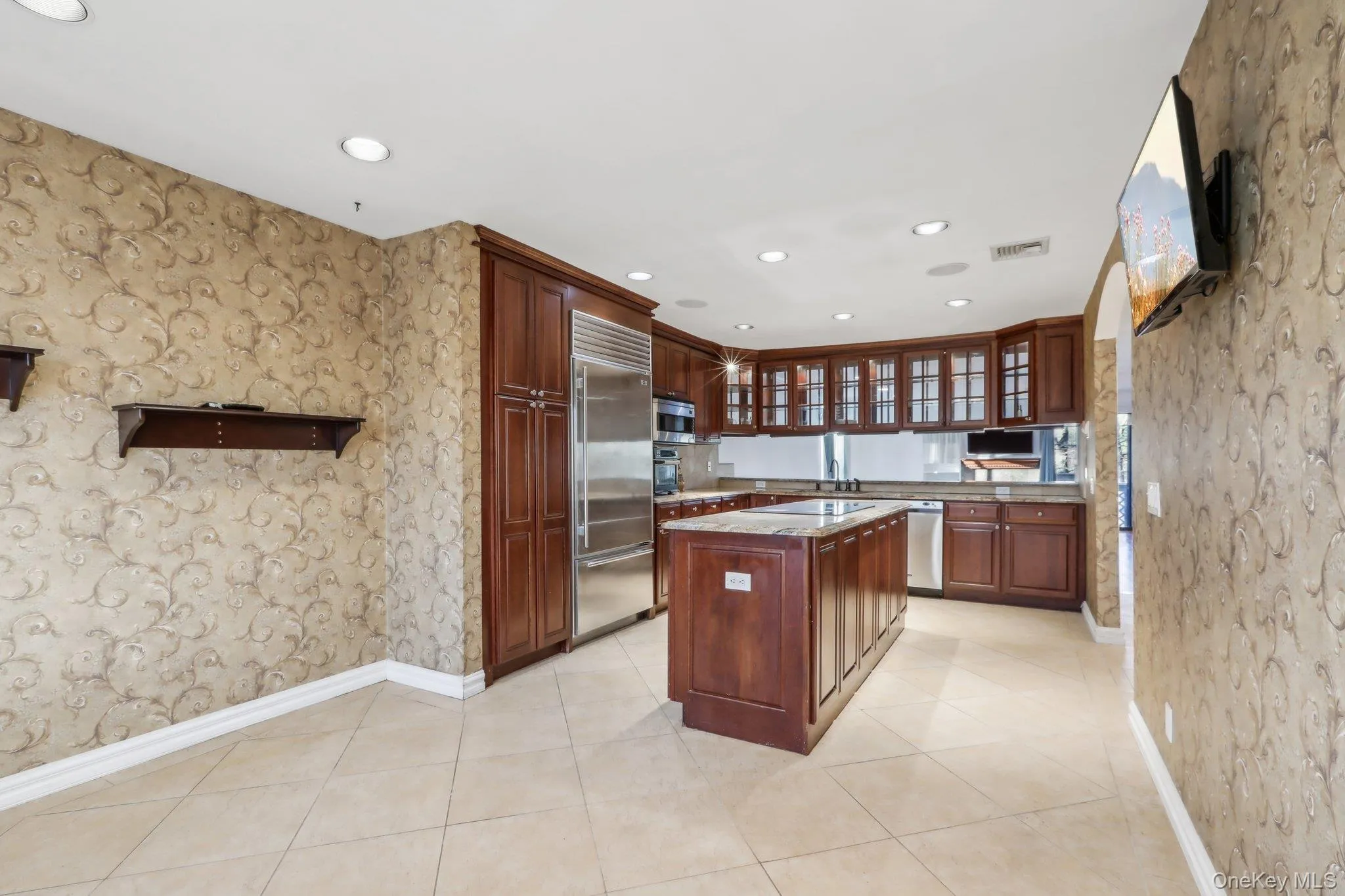 Kitchen with wallpapered walls, glass insert cabinets, a kitchen island, stainless steel appliances, and recessed lighting Kitchen with wallpapered walls, glass insert cabinets, a kitchen island, stainless steel appliances, and recessed lighting