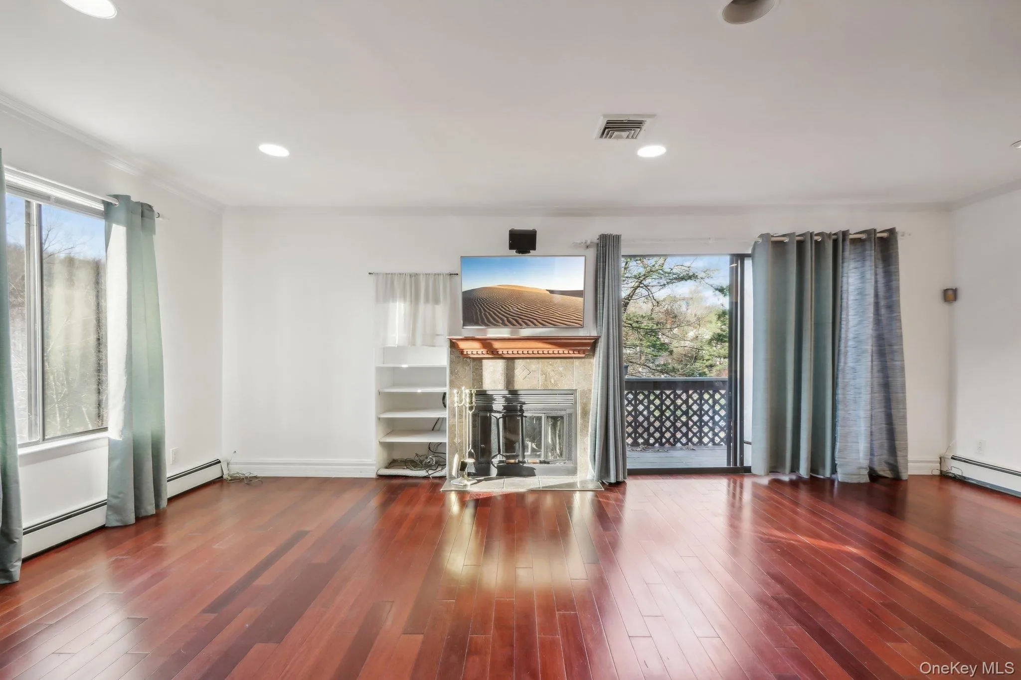Unfurnished living room with wood finished floors, a fireplace, recessed lighting, ornamental molding, and a baseboard radiator Unfurnished living room with wood finished floors, a fireplace, recessed lighting, ornamental molding, and a baseboard radiator
