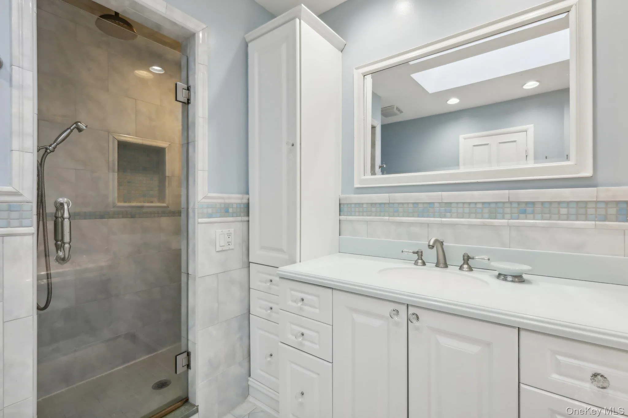 Full bath with tile walls, a stall shower, vanity, a skylight, and a wainscoted wall Full bath with tile walls, a stall shower, vanity, a skylight, and a wainscoted wall