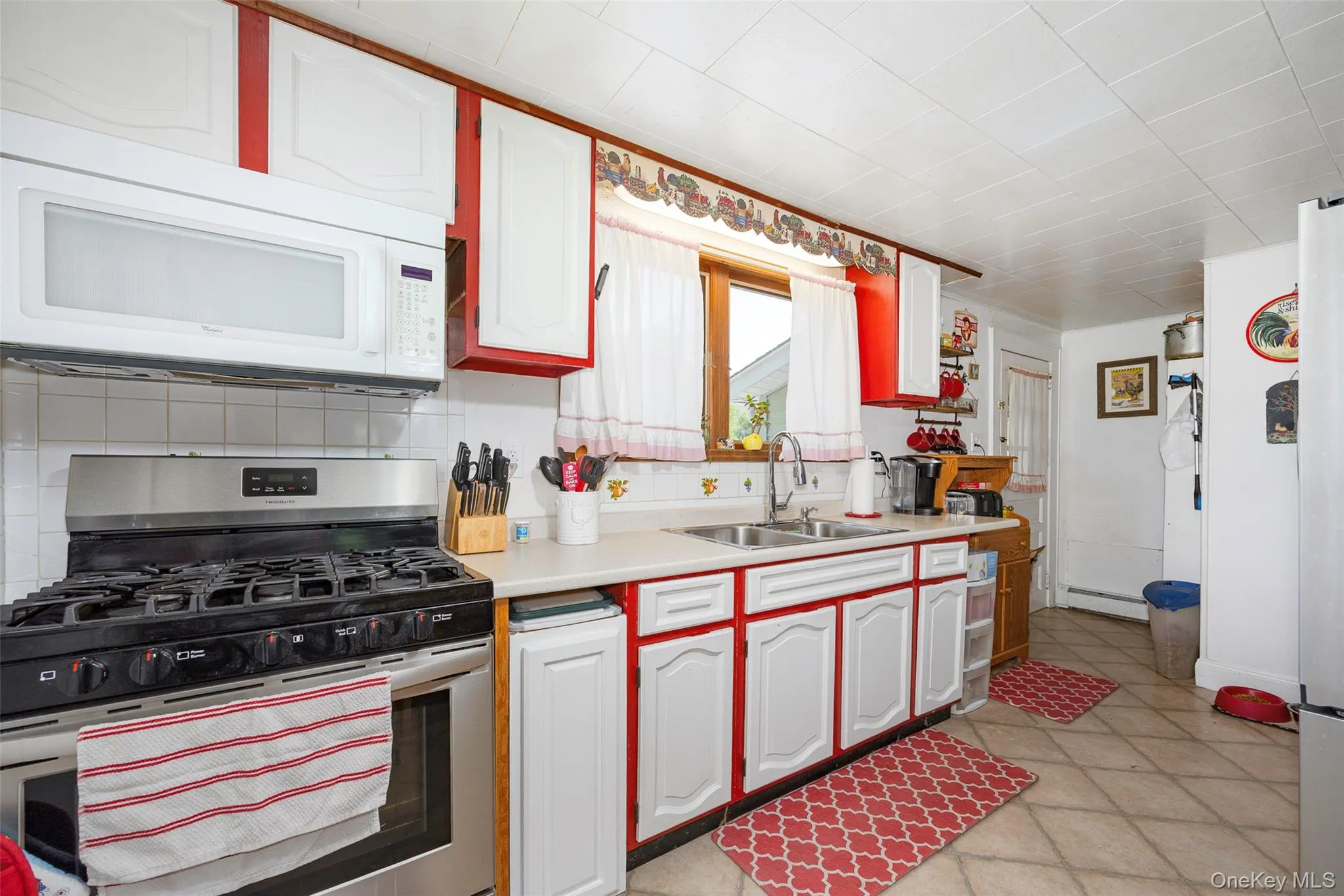 Kitchen with stainless steel gas stove, light countertops, white microwave, white cabinets, and baseboard heating Kitchen with stainless steel gas stove, light countertops, white microwave, white cabinets, and baseboard heating