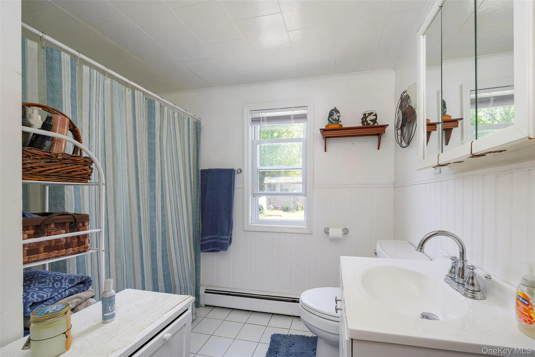 Full bathroom featuring wainscoting, a baseboard heating unit, vanity, tile patterned floors, and a shower with curtain Full bathroom featuring wainscoting, a baseboard heating unit, vanity, tile patterned floors, and a shower with curtain