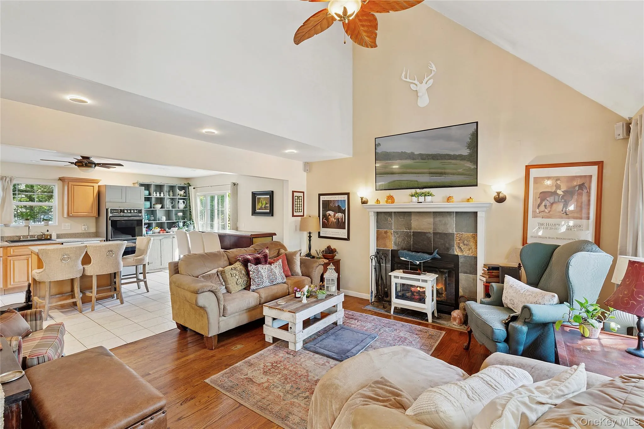 Living room featuring a fireplace, ceiling fan, light wood-type flooring, and high vaulted ceiling Living room featuring a fireplace, ceiling fan, light wood-type flooring, and high vaulted ceiling
