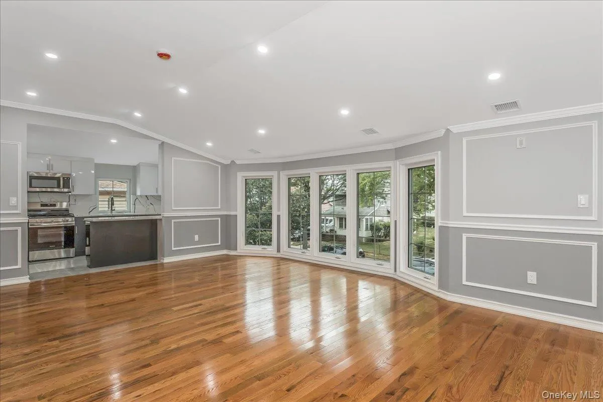 Unfurnished living room featuring plenty of natural light, light wood finished floors, a decorative wall, ornamental molding, and vaulted ceiling Unfurnished living room featuring plenty of natural light, light wood finished floors, a decorative wall, ornamental molding, and vaulted ceiling