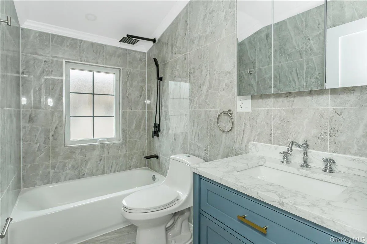 Bathroom featuring tile walls, shower / bath combination, vanity, and ornamental molding Bathroom featuring tile walls, shower / bath combination, vanity, and ornamental molding