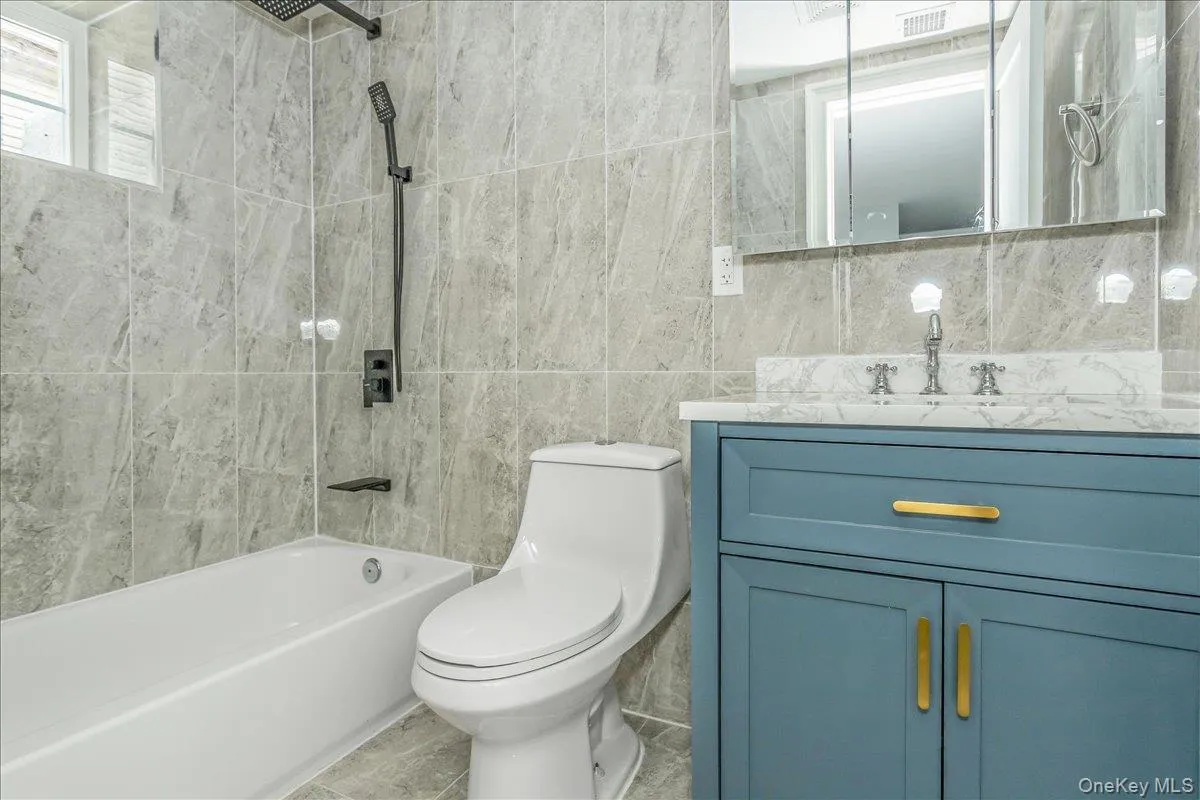 Full bathroom featuring bathing tub / shower combination, vanity, tile walls, and tile patterned flooring Full bathroom featuring bathing tub / shower combination, vanity, tile walls, and tile patterned flooring