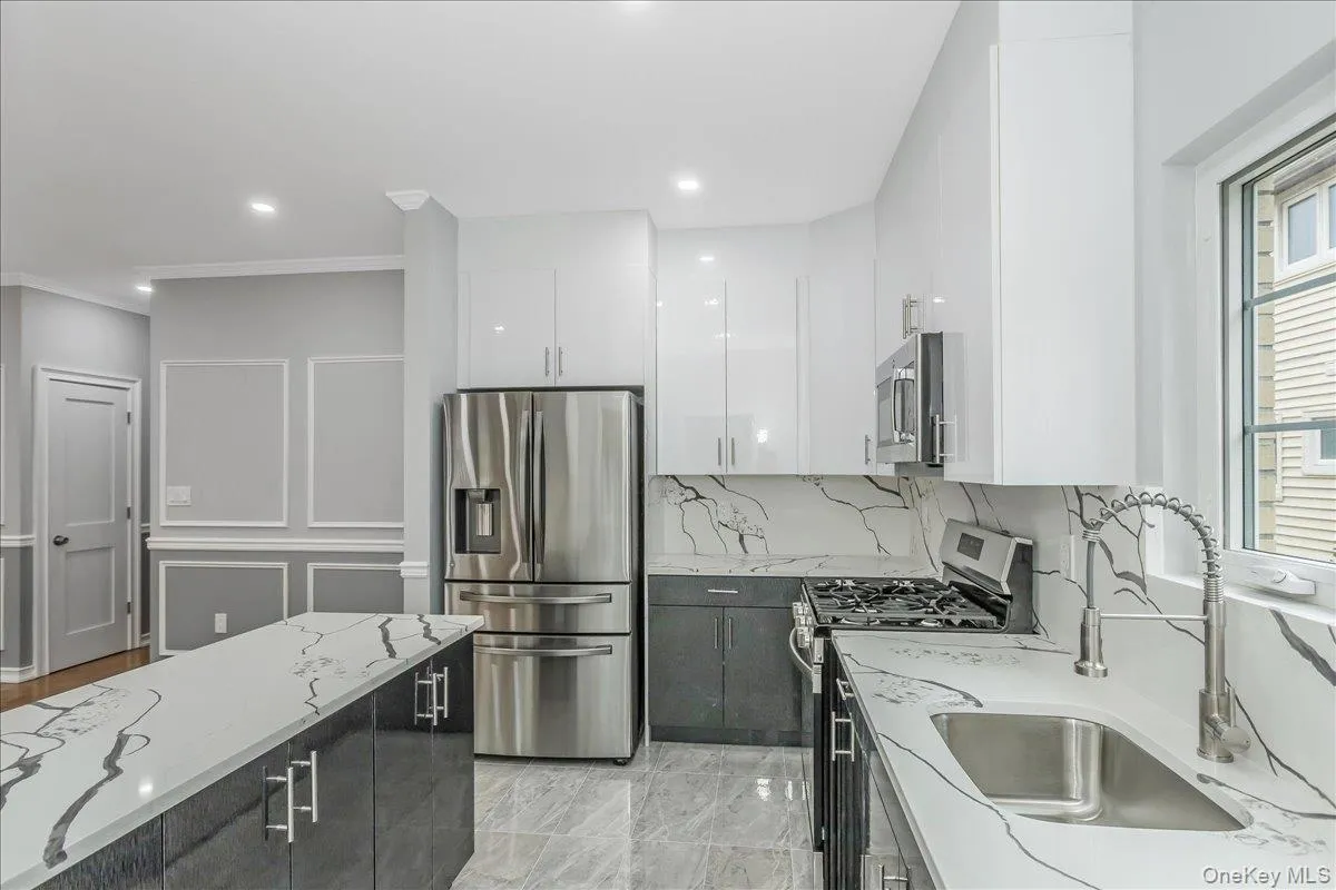 Kitchen with appliances with stainless steel finishes, white cabinets, modern cabinets, light stone countertops, and dark cabinetry Kitchen with appliances with stainless steel finishes, white cabinets, modern cabinets, light stone countertops, and dark cabinetry