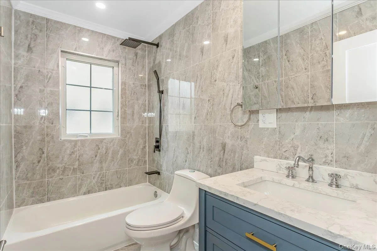Bathroom with bathing tub / shower combination, tile walls, vanity, and ornamental molding Bathroom with bathing tub / shower combination, tile walls, vanity, and ornamental molding