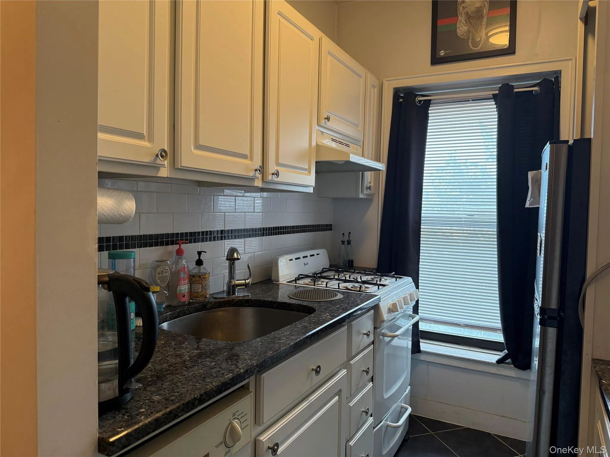Kitchen featuring white range with gas stovetop, dark stone counters, backsplash, white cabinets, and under cabinet range hood Kitchen featuring white range with gas stovetop, dark stone counters, backsplash, white cabinets, and under cabinet range hood