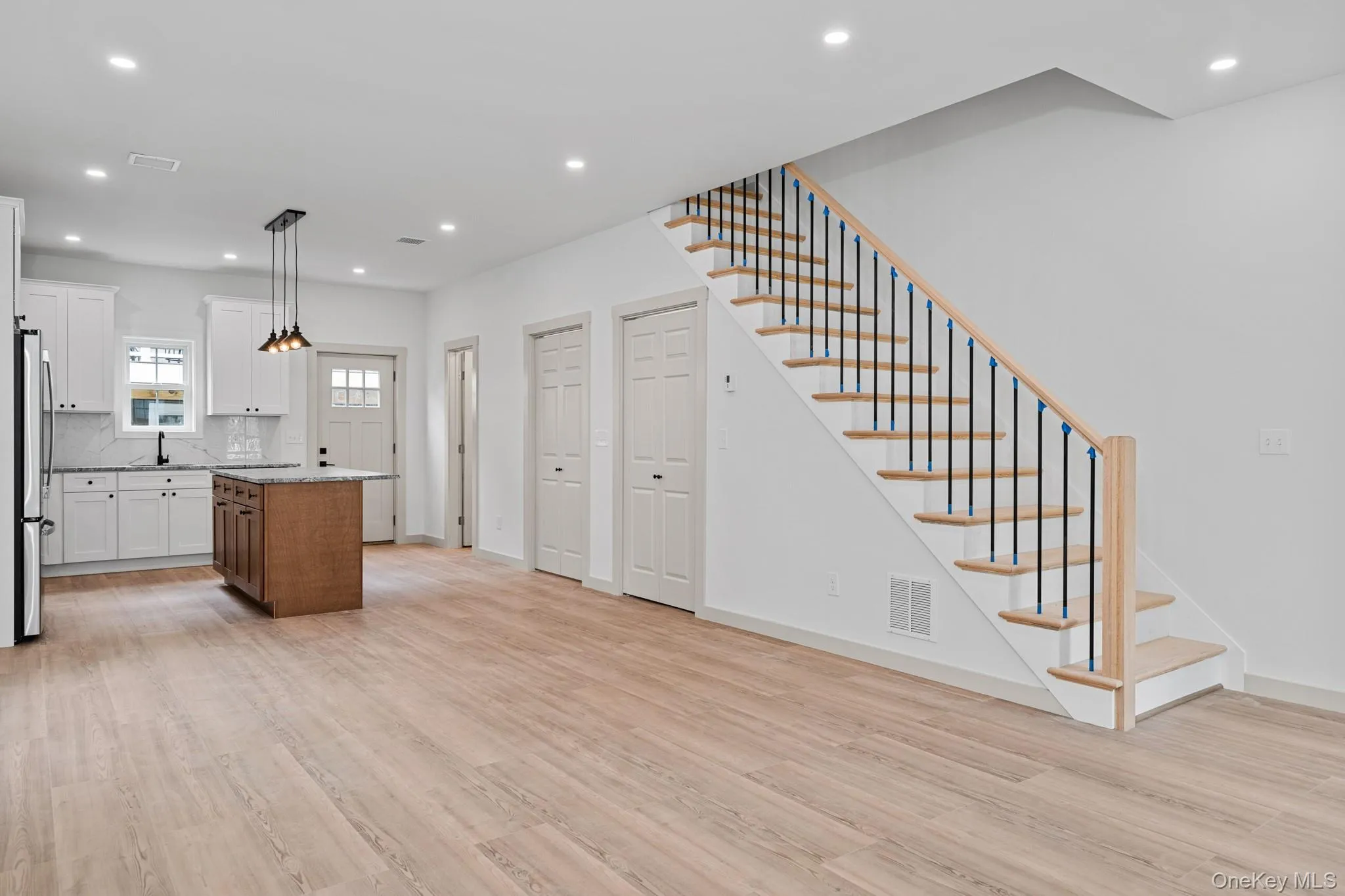Kitchen featuring light wood-type flooring, recessed lighting, white cabinets, backsplash, and hanging light fixtures Kitchen featuring light wood-type flooring, recessed lighting, white cabinets, backsplash, and hanging light fixtures