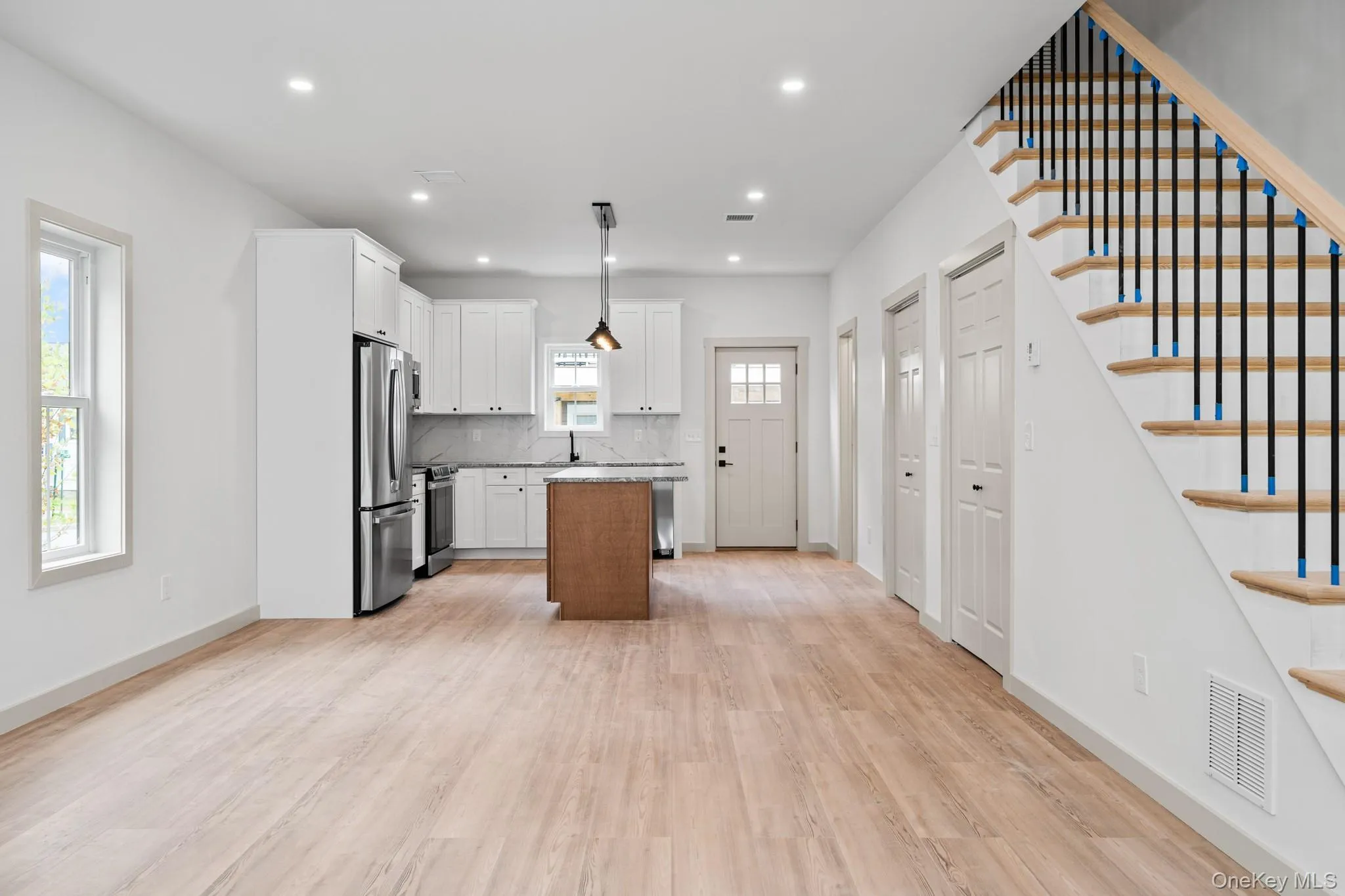 Kitchen with a center island, backsplash, white cabinetry, light wood-type flooring, and stainless steel appliances Kitchen with a center island, backsplash, white cabinetry, light wood-type flooring, and stainless steel appliances