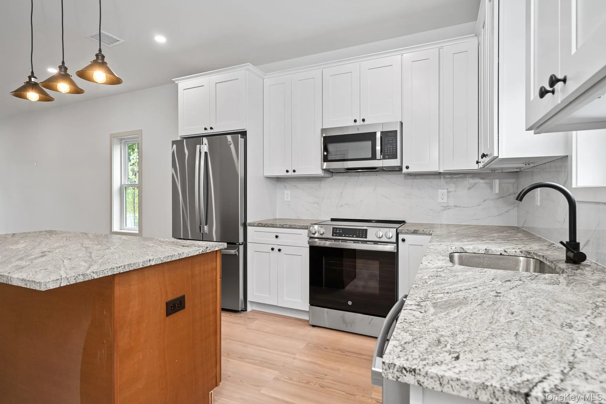 Kitchen featuring stainless steel appliances, backsplash, decorative light fixtures, light stone counters, and white cabinetry Kitchen featuring stainless steel appliances, backsplash, decorative light fixtures, light stone counters, and white cabinetry