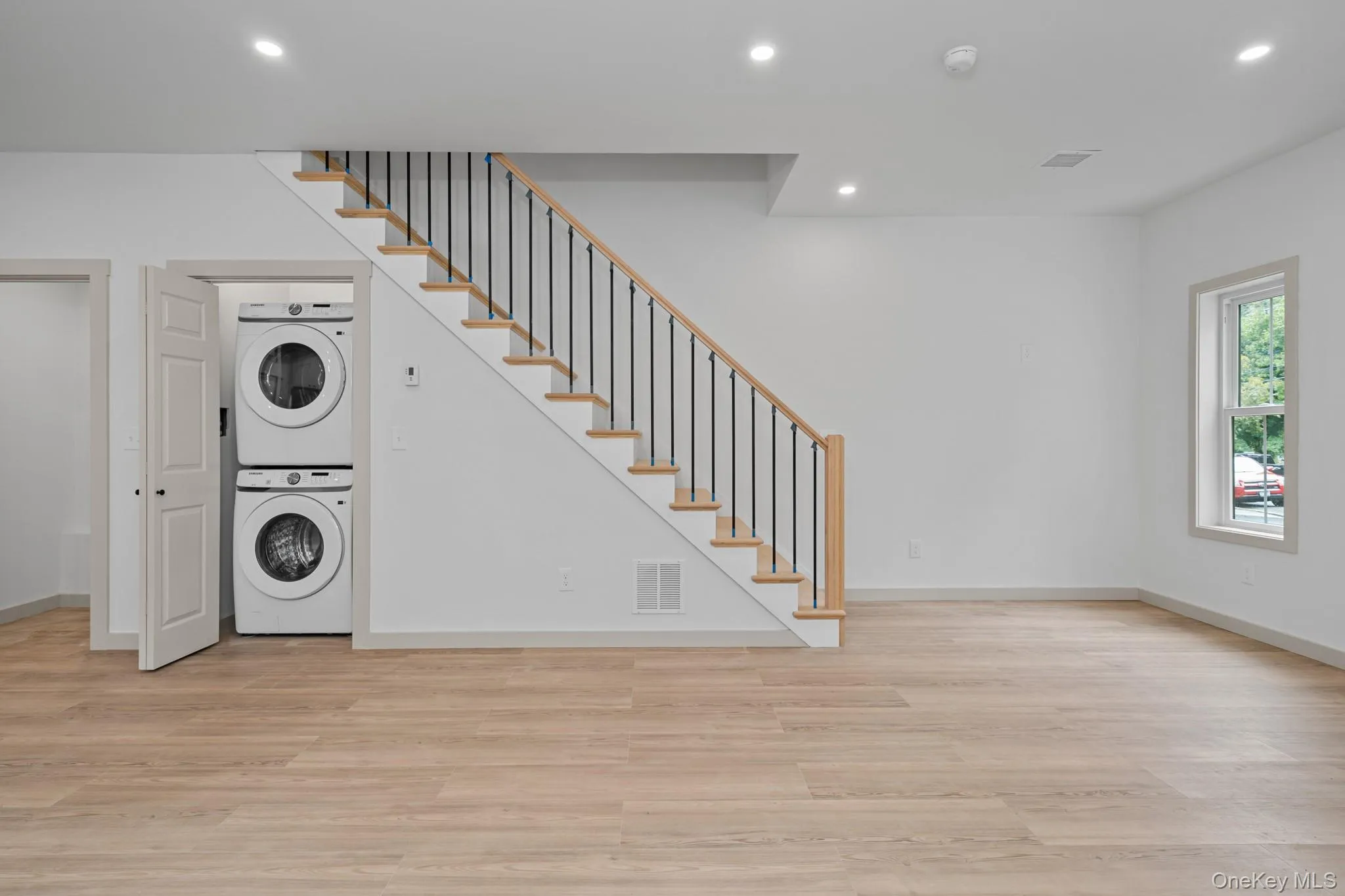 Washroom with recessed lighting, light wood finished floors, and stacked washing machine and dryer Washroom with recessed lighting, light wood finished floors, and stacked washing machine and dryer