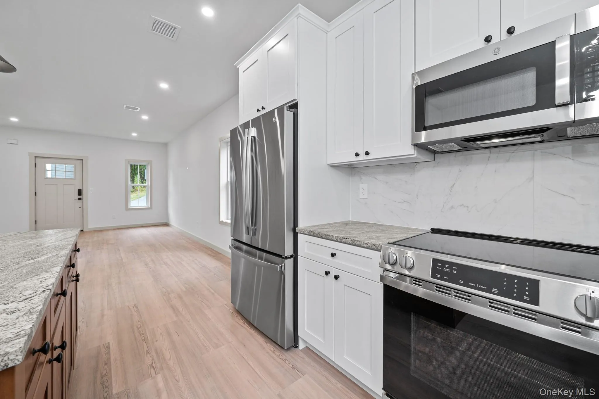 Kitchen featuring appliances with stainless steel finishes, recessed lighting, light stone counters, light wood-style floors, and white cabinetry Kitchen featuring appliances with stainless steel finishes, recessed lighting, light stone counters, light wood-style floors, and white cabinetry