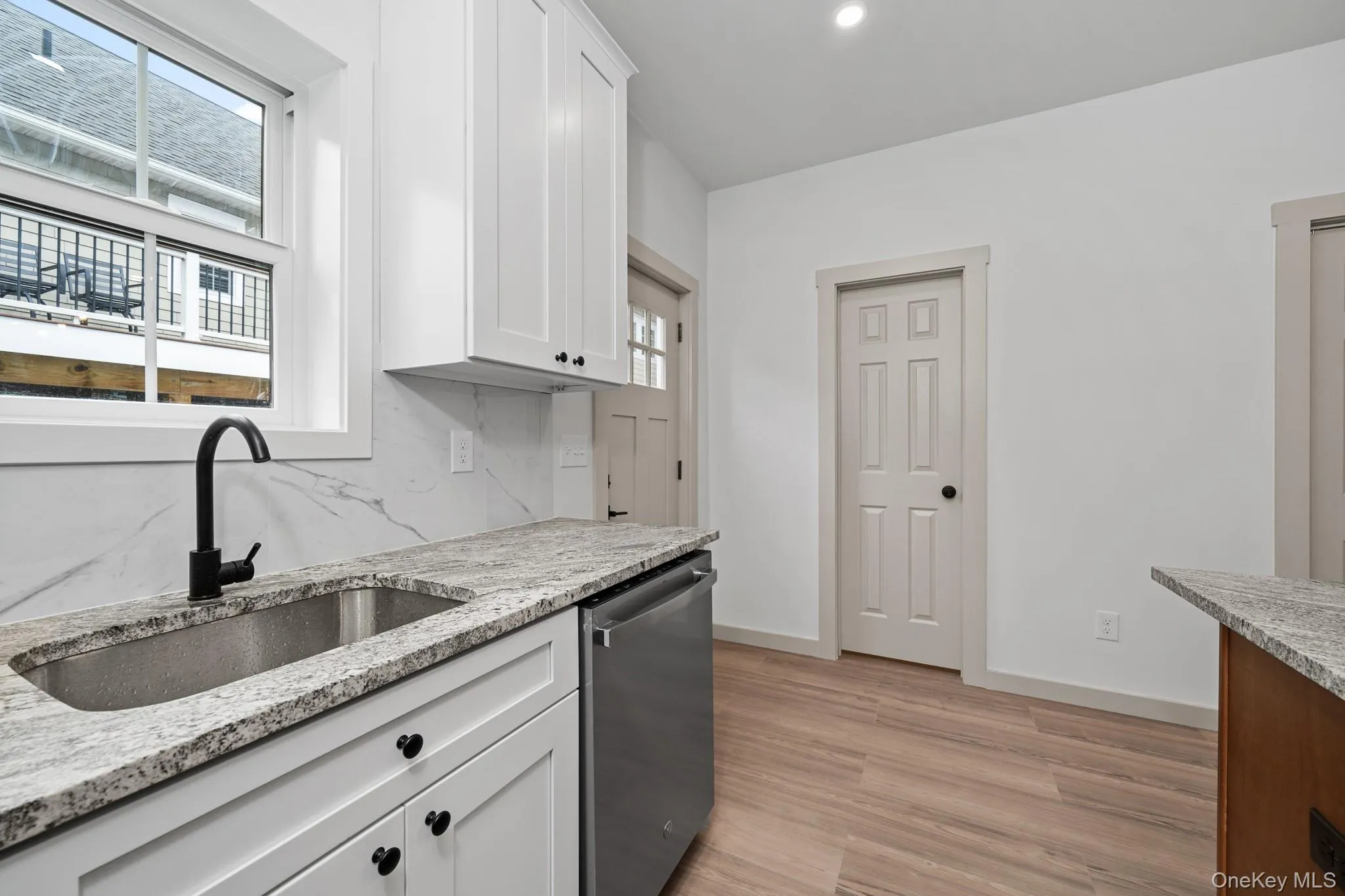 Kitchen featuring dishwasher, light wood-style floors, light stone counters, white cabinetry, and tasteful backsplash Kitchen featuring dishwasher, light wood-style floors, light stone counters, white cabinetry, and tasteful backsplash