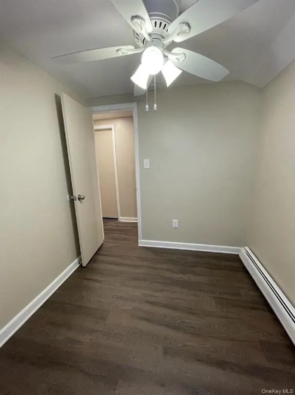 Spare room with a baseboard heating unit, dark wood-style flooring, and ceiling fan Spare room with a baseboard heating unit, dark wood-style flooring, and ceiling fan