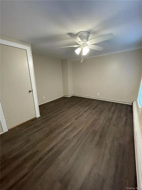 Empty room with dark wood-style flooring, a ceiling fan, and a baseboard radiator Empty room with dark wood-style flooring, a ceiling fan, and a baseboard radiator