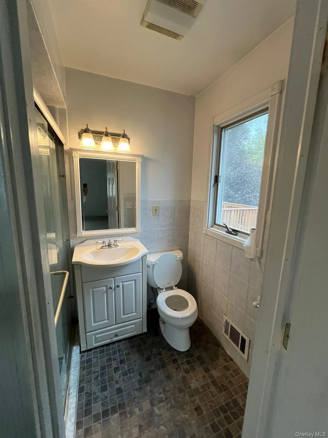 Full bath featuring tile walls, vanity, dark tile patterned flooring, and a wainscoted wall Full bath featuring tile walls, vanity, dark tile patterned flooring, and a wainscoted wall