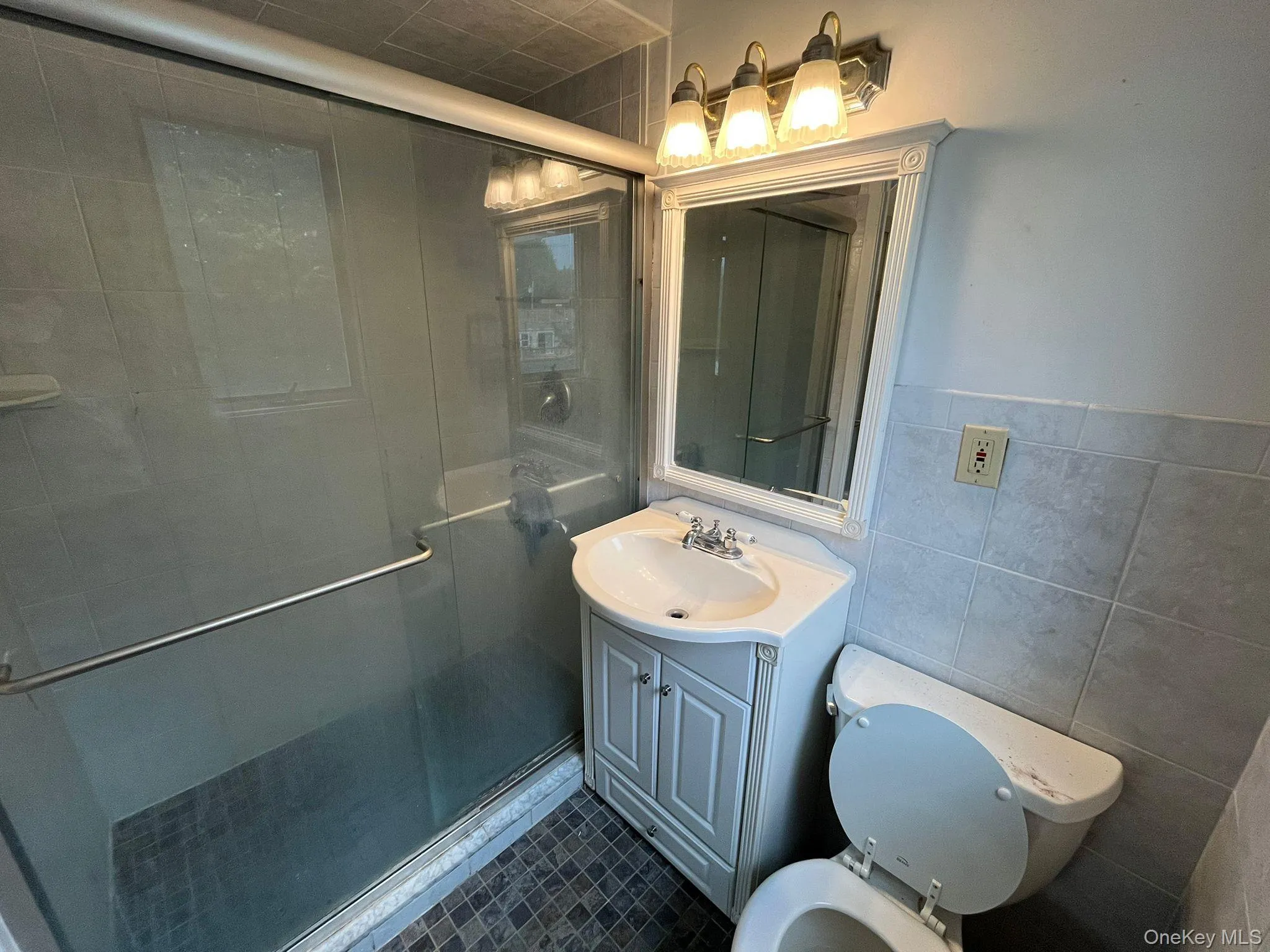 Full bath with a shower stall, tile walls, vanity, and dark tile patterned floors Full bath with a shower stall, tile walls, vanity, and dark tile patterned floors