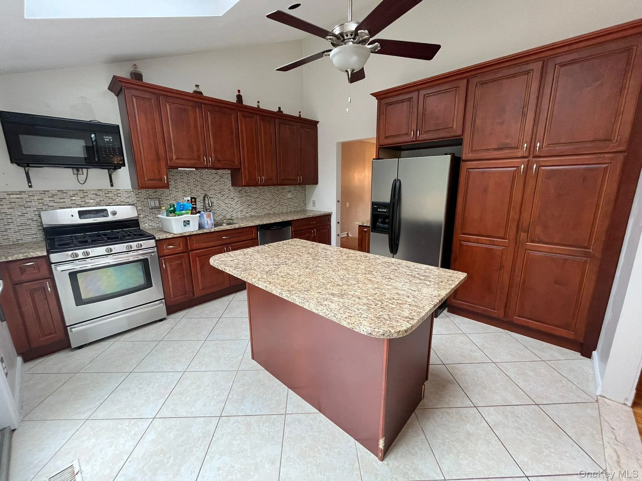 Kitchen featuring stainless steel appliances, decorative backsplash, light tile patterned floors, a ceiling fan, and a skylight Kitchen featuring stainless steel appliances, decorative backsplash, light tile patterned floors, a ceiling fan, and a skylight