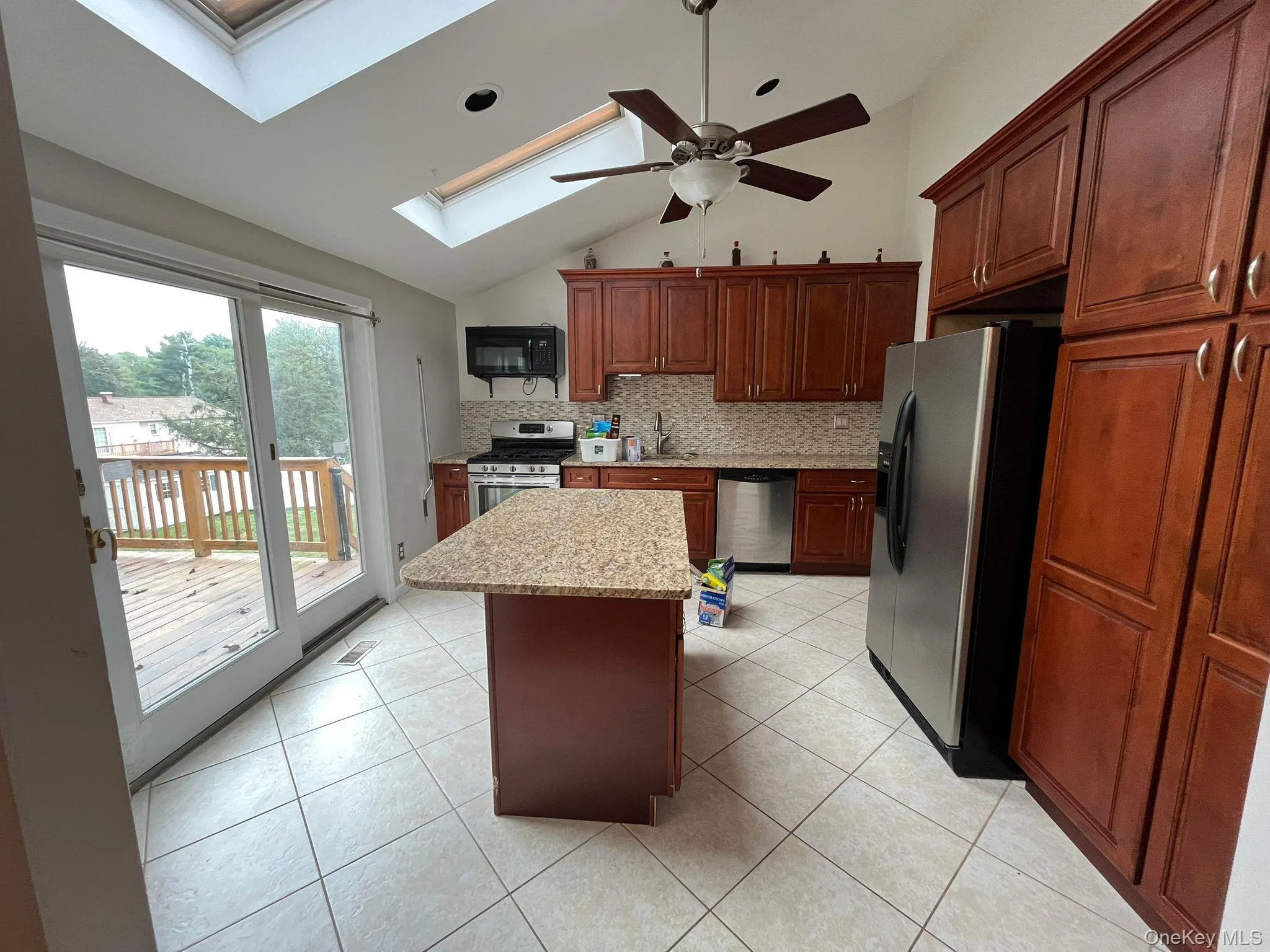 Kitchen featuring stainless steel appliances, decorative backsplash, a center island, a skylight, and light tile patterned floors Kitchen featuring stainless steel appliances, decorative backsplash, a center island, a skylight, and light tile patterned floors