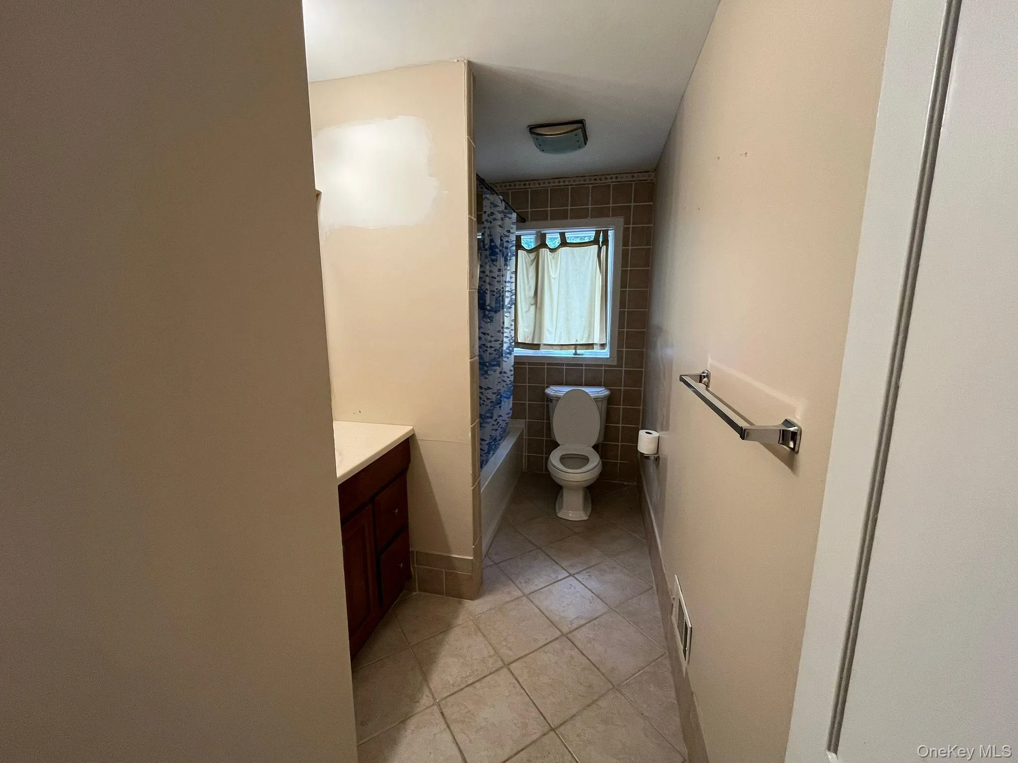 Full bath featuring light tile patterned floors, vanity, shower / bath combination with curtain, and tile walls Full bath featuring light tile patterned floors, vanity, shower / bath combination with curtain, and tile walls