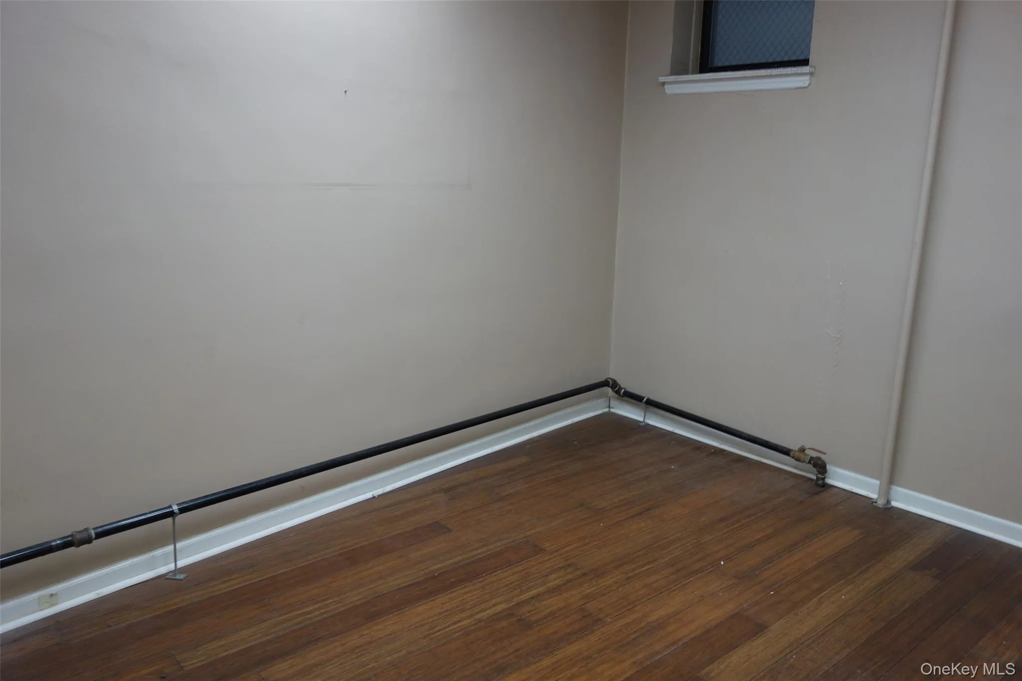 Empty room with dark wood-style flooring and baseboards Empty room with dark wood-style flooring and baseboards